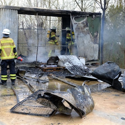 Feuerwehrleute stehen in Mechernich vor und in einem Wohncontainer, der durch einen Brand völlig zerstört worden ist.