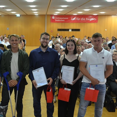 Fünf junge Männer und eine Frau stehen in einem großen Saal und halten eine Urkunde in den Händen. Im Hintergrund ist Publikum zu erkennen.
