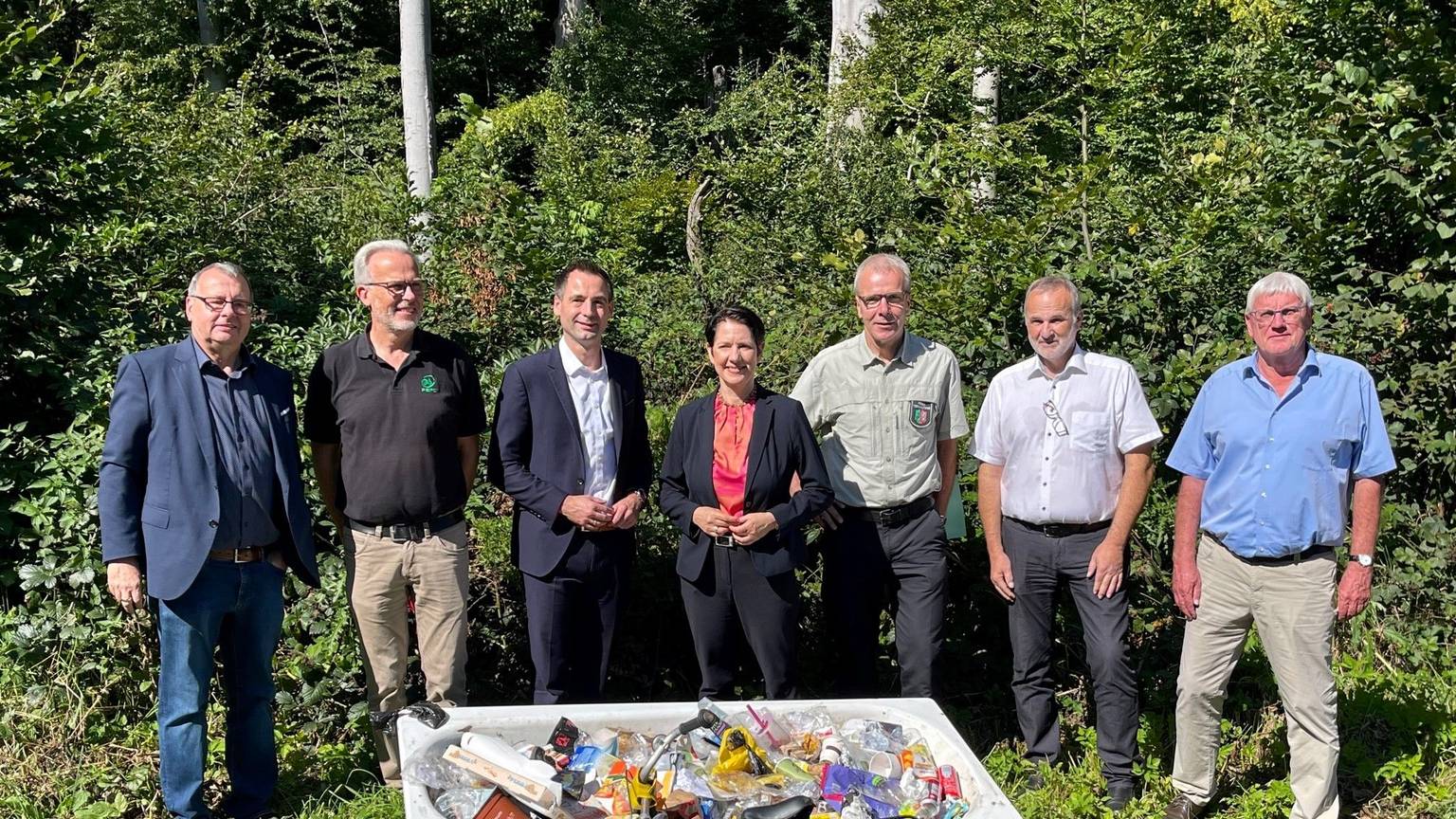 Eine Badewanne voller Müll im Kottenforst, dahinter Ministerin Silke Gorißen