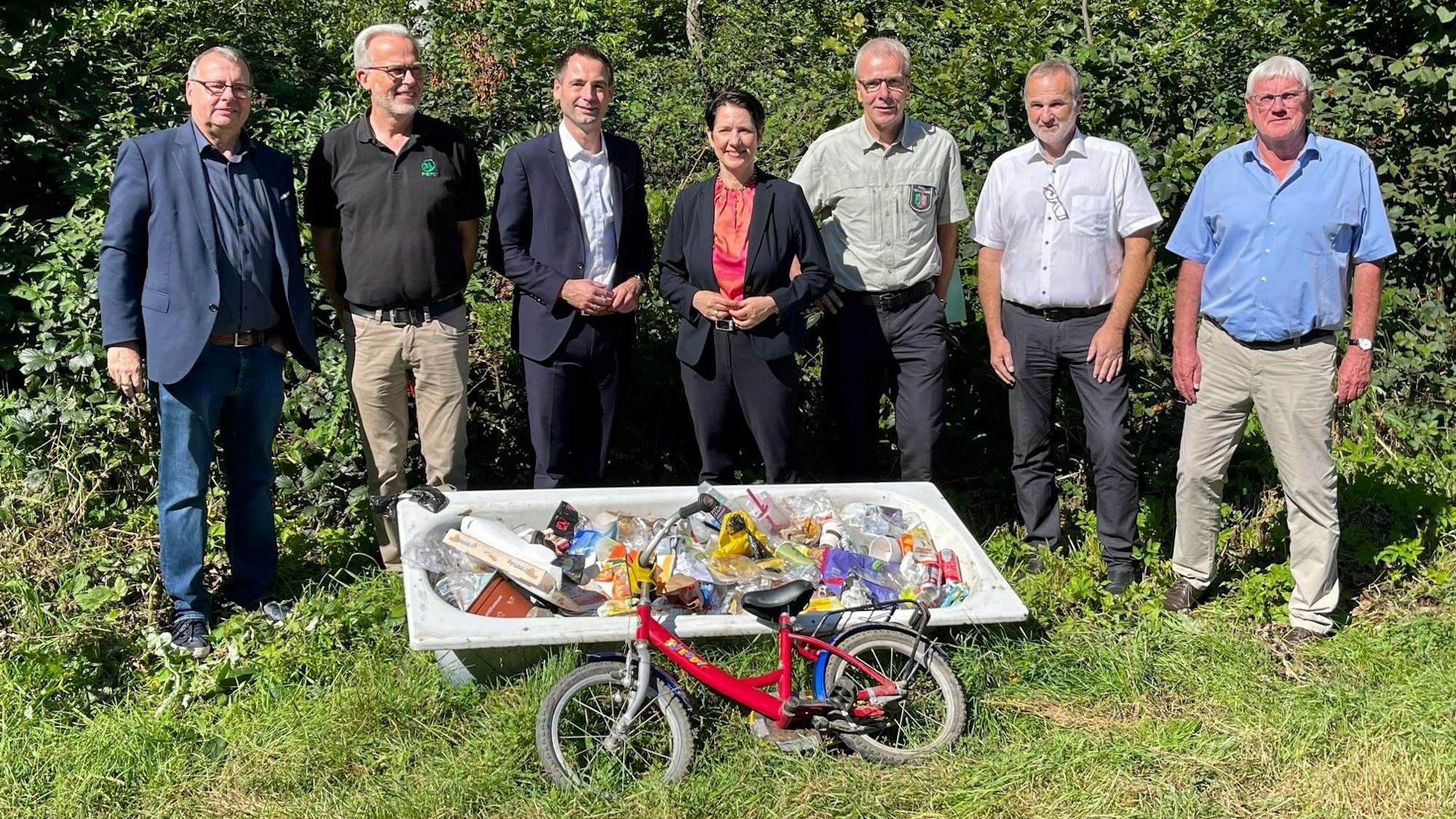 Eine Badewanne voller Müll im Kottenforst, dahinter Ministerin Silke Gorißen