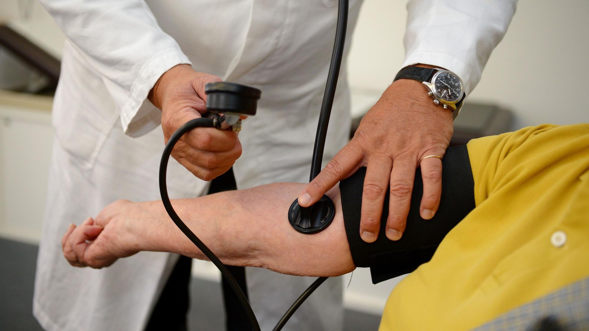 Ein Hausarzt misst einer Patientin den Blutdruck.