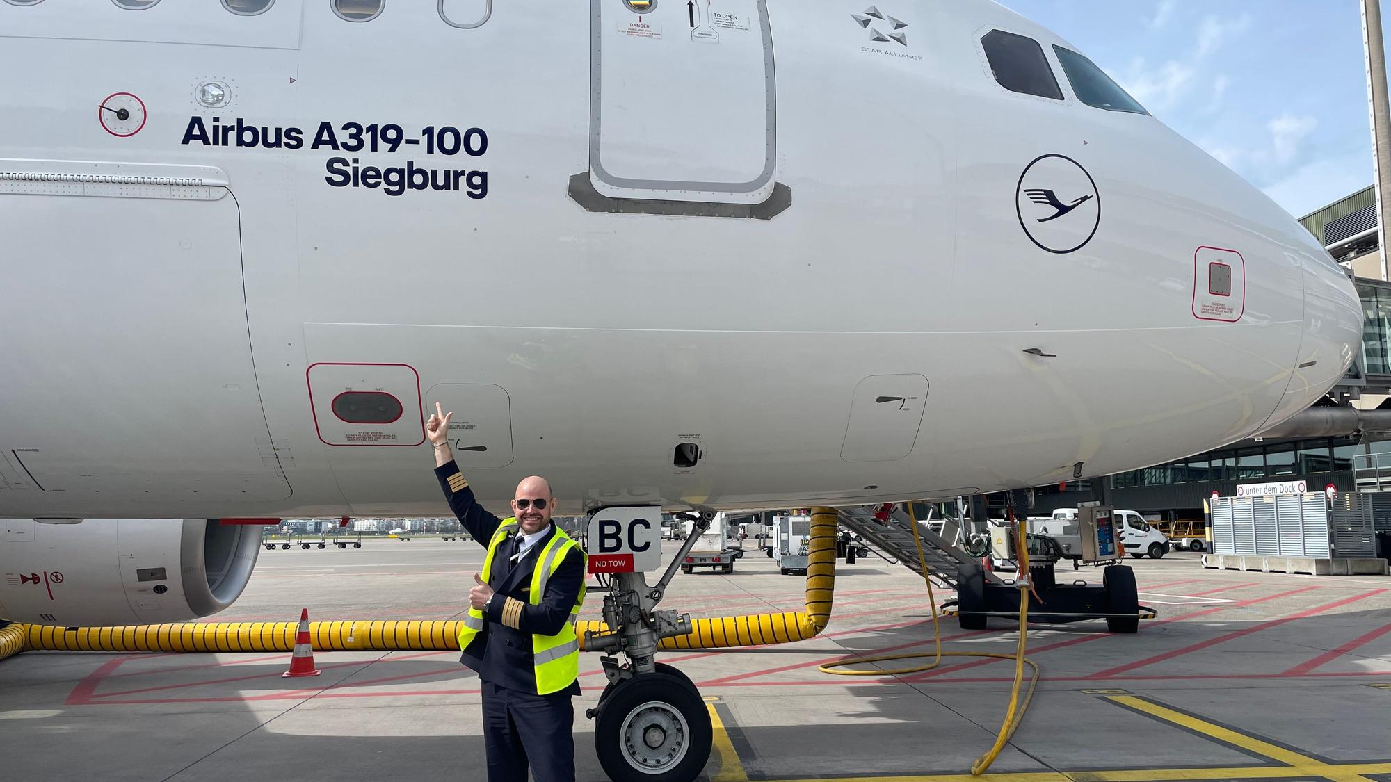 Ein Pilot steht auf dem Rollfeld vor einem Flugzeug.