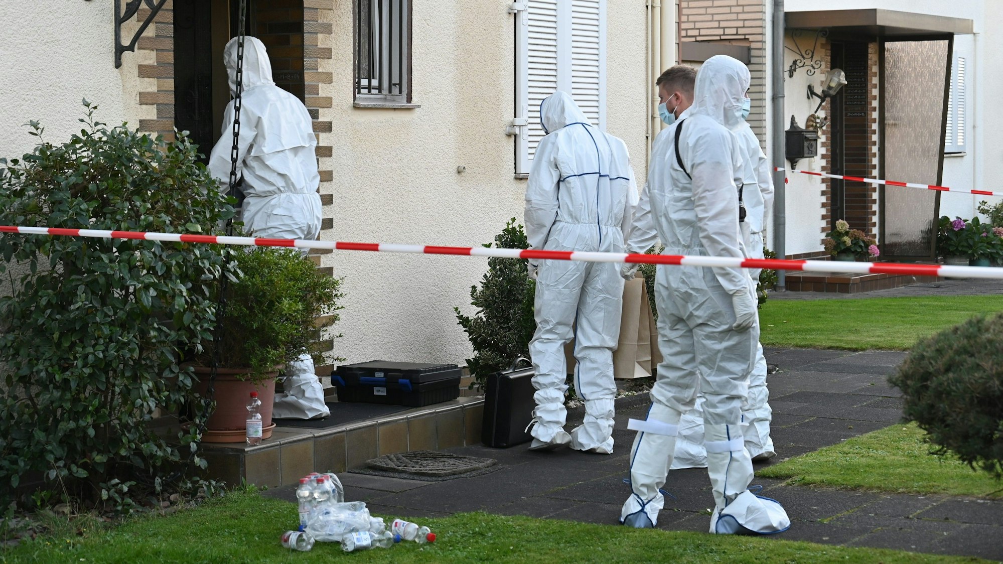 Das Bild zeigt Polizeibeamte in weißen Schutzanzügen am Tatort.