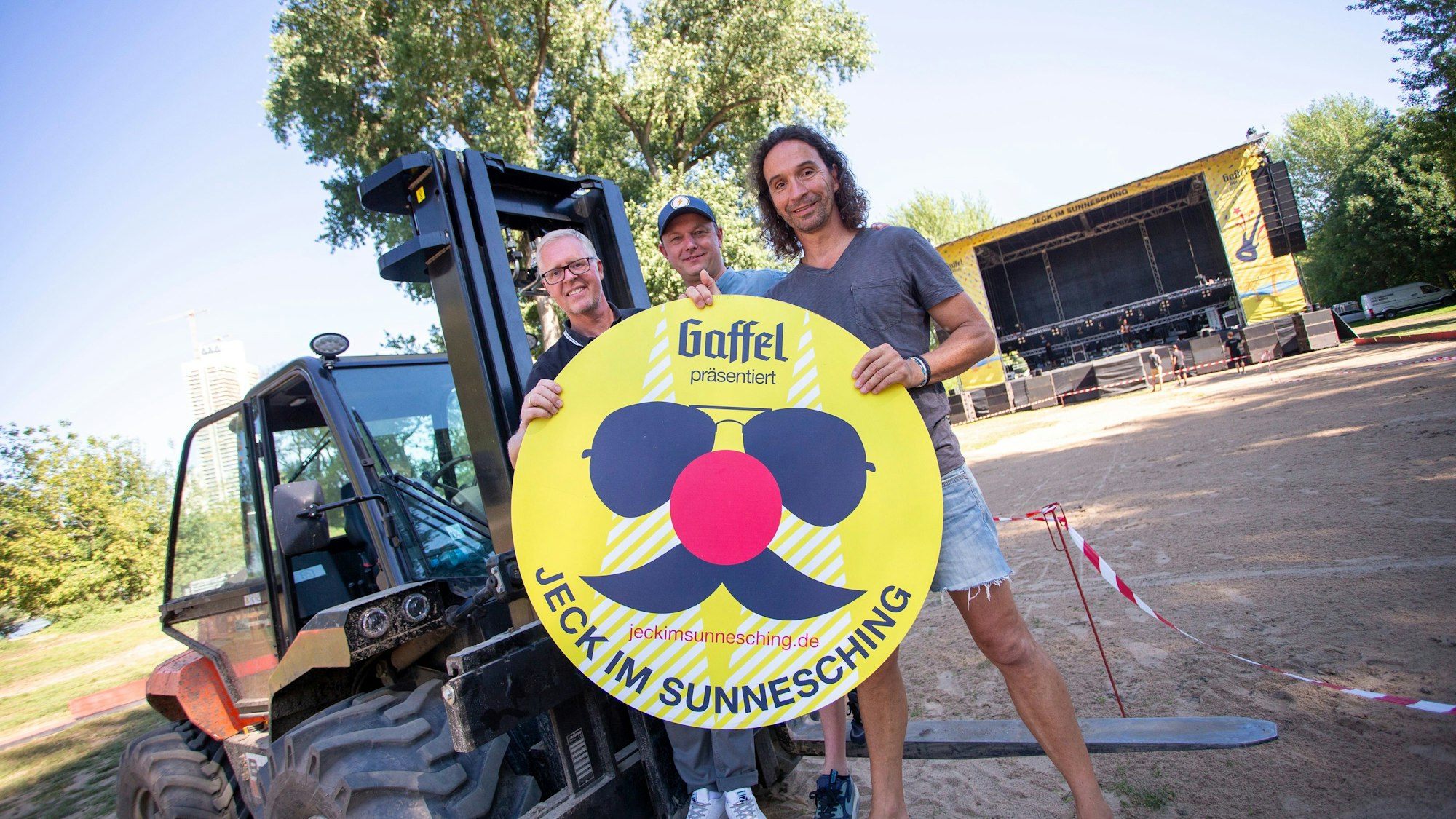 Thomas Deloy, Jochen Gasser und Stephan Brings (v.l.) stehen vor einem Gabelstapler, der vor einer großen Bühne steht.