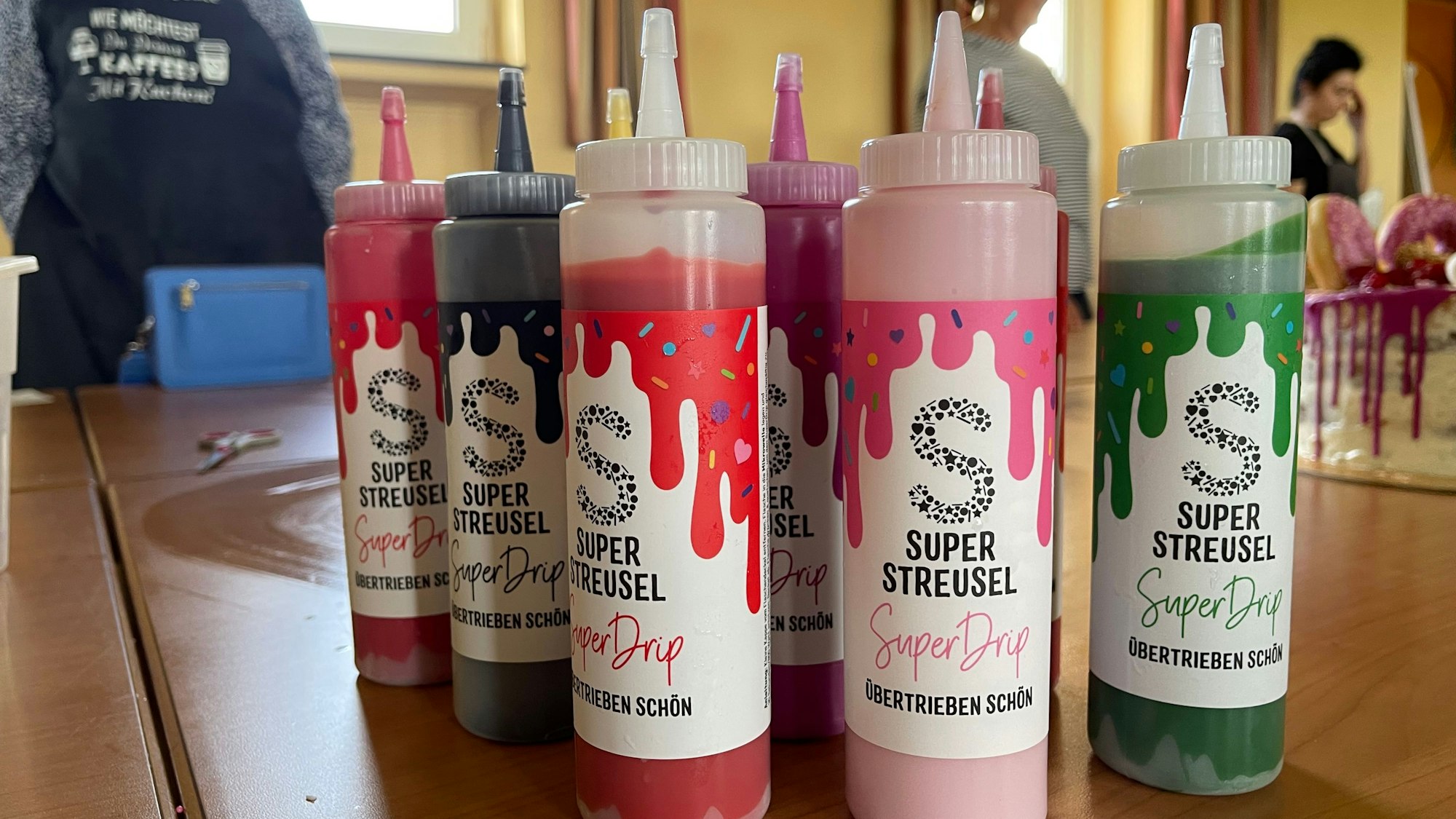 Gummiflaschen mit bunter Flüssigkeit und der Aufschrift „Super Drip “stehen auf einem Tisch.