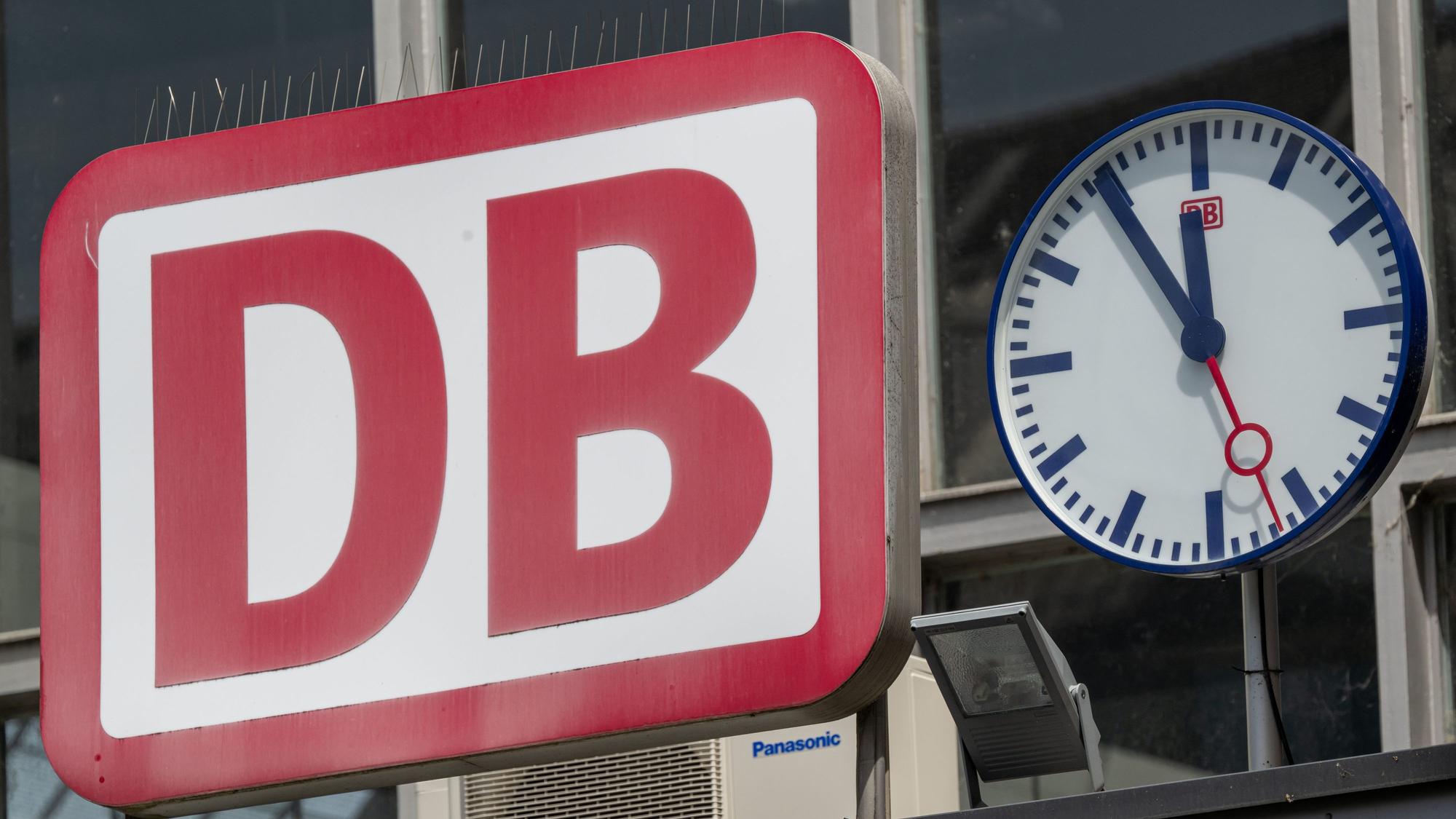 Die Uhr neben dem Logo der Deutschen Bahn (DB) zeigt am Eingang zum Münchner Hauptbahnhof auf „Fünf vor Zwölf“. (Symbolbild)