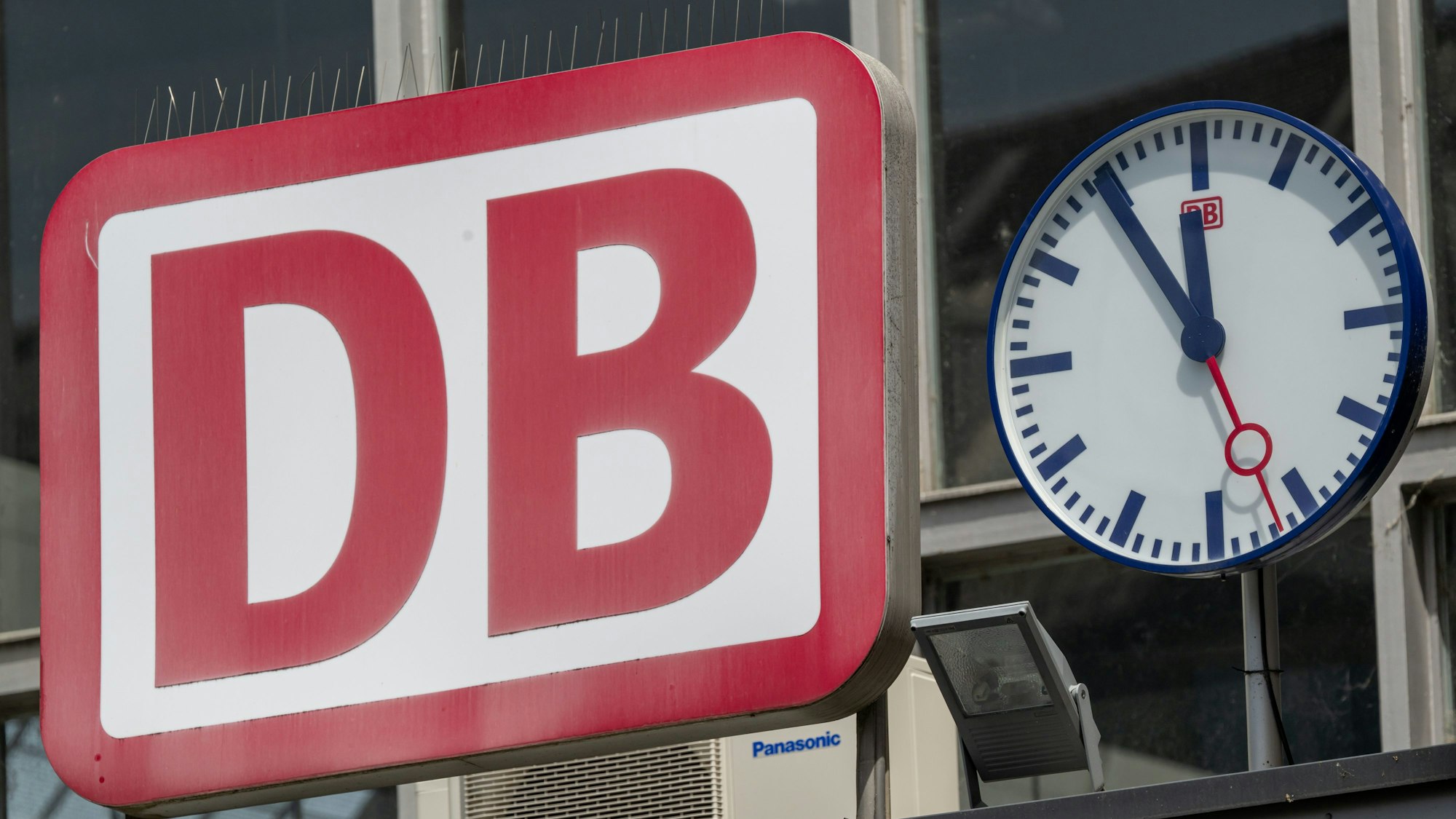 Die Uhr neben dem Logo der Deutschen Bahn (DB) zeigt am Eingang zum Münchner Hauptbahnhof auf „Fünf vor Zwölf“. (Symbolbild)