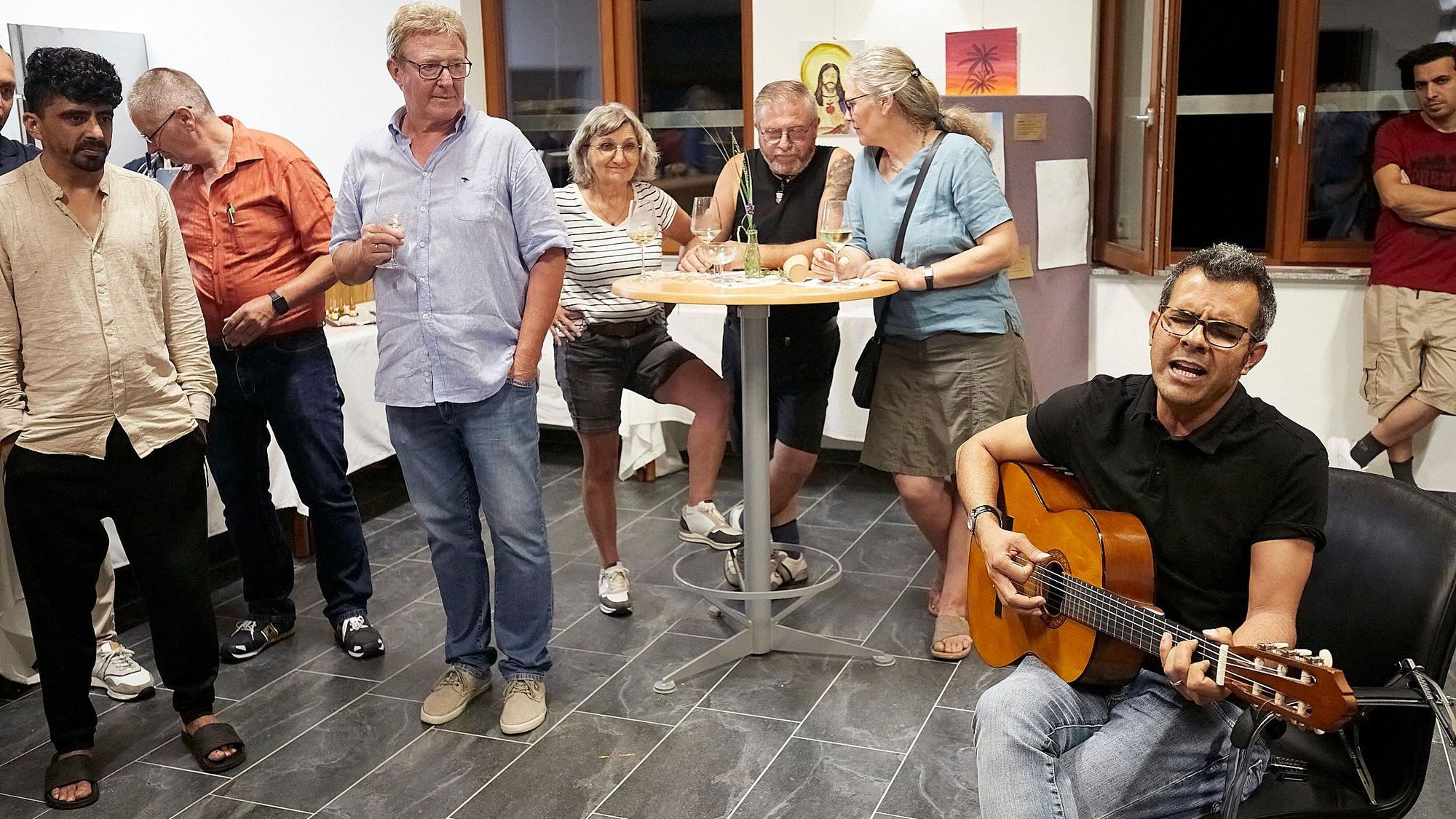 Ahmad Abbaspour singt und spielt Gitarre. Einige Zuhörer stehen um ihn herum.
