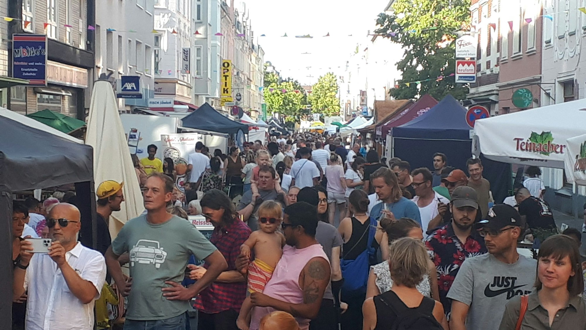 Viele Menschen drängen sich auf einer Straße, rechts und links sind Sonnenschirme und Zelte aufgebaut.