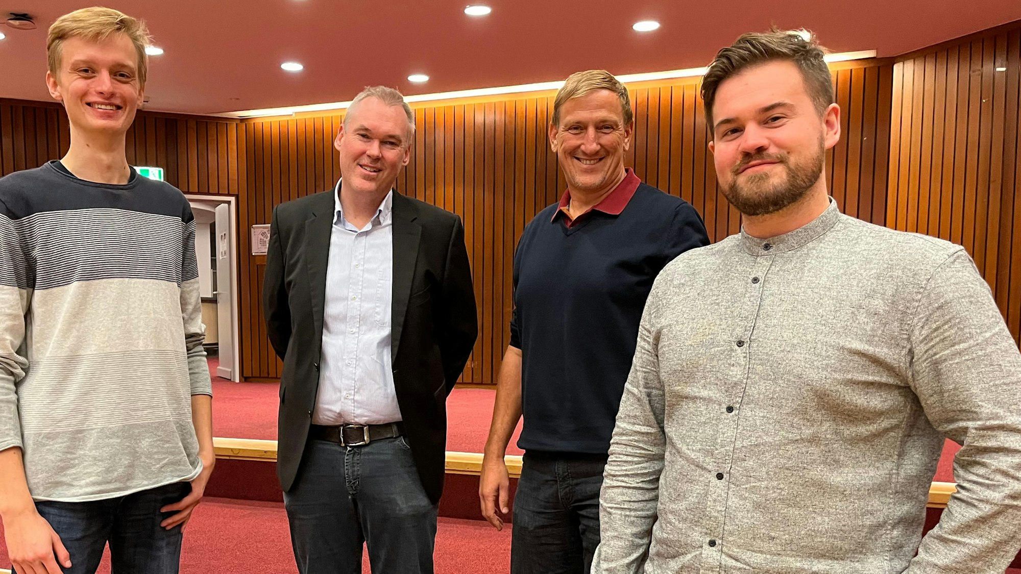 Ein junger Mann mit Bart posiert neben drei anderen Herren.