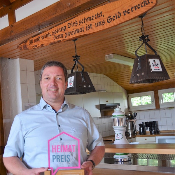 Stolz präsentiert Jan Wirths, Vorsitzender des Trägervereins „Alter Schulbezirk Wallerhausen“, den Heimat-Preis, den sein Verein 2021 für ein erstes Projekt am Dörfergemeinschaftshaus in Morsbach-Wallerhausen erhalten hat. Wirths steht in dem Saal, der künftig auch vermietet werden soll.