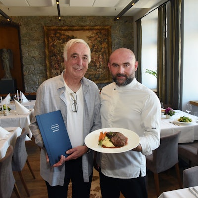 Klaus Ortlieb und Armend Mustafi stehen im Gastraum des „Hotels am Markt“ in Wipperfürth und zeigen ein Gericht von der neuen Speisekarte.