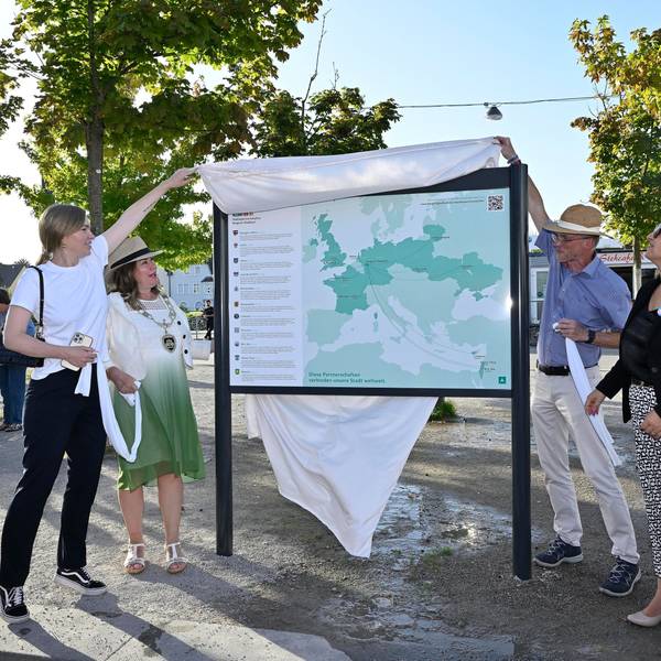 Vier Menschen enthüllen eine neue Tafel am „Platz der Partnerstädte“ in Bergisch Gladbach.