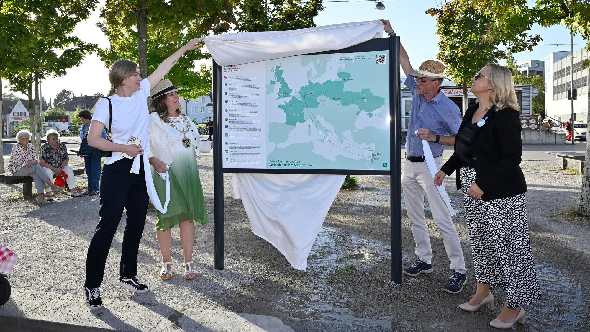 Vier Menschen enthüllen eine neue Tafel am „Platz der Partnerstädte“ in Bergisch Gladbach.