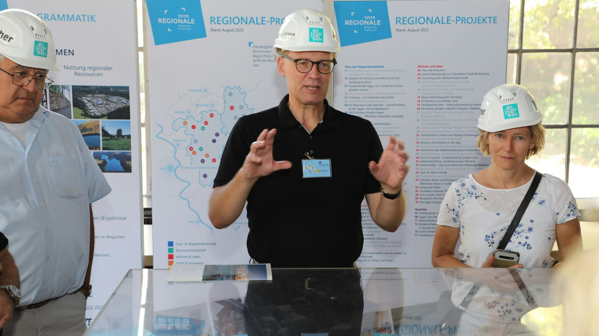 Ein Mann in schwarzem T-Shirt erläutert einer Gruppe etwas vor einer Wand des Strukturförderprogramms Regionale 2025.