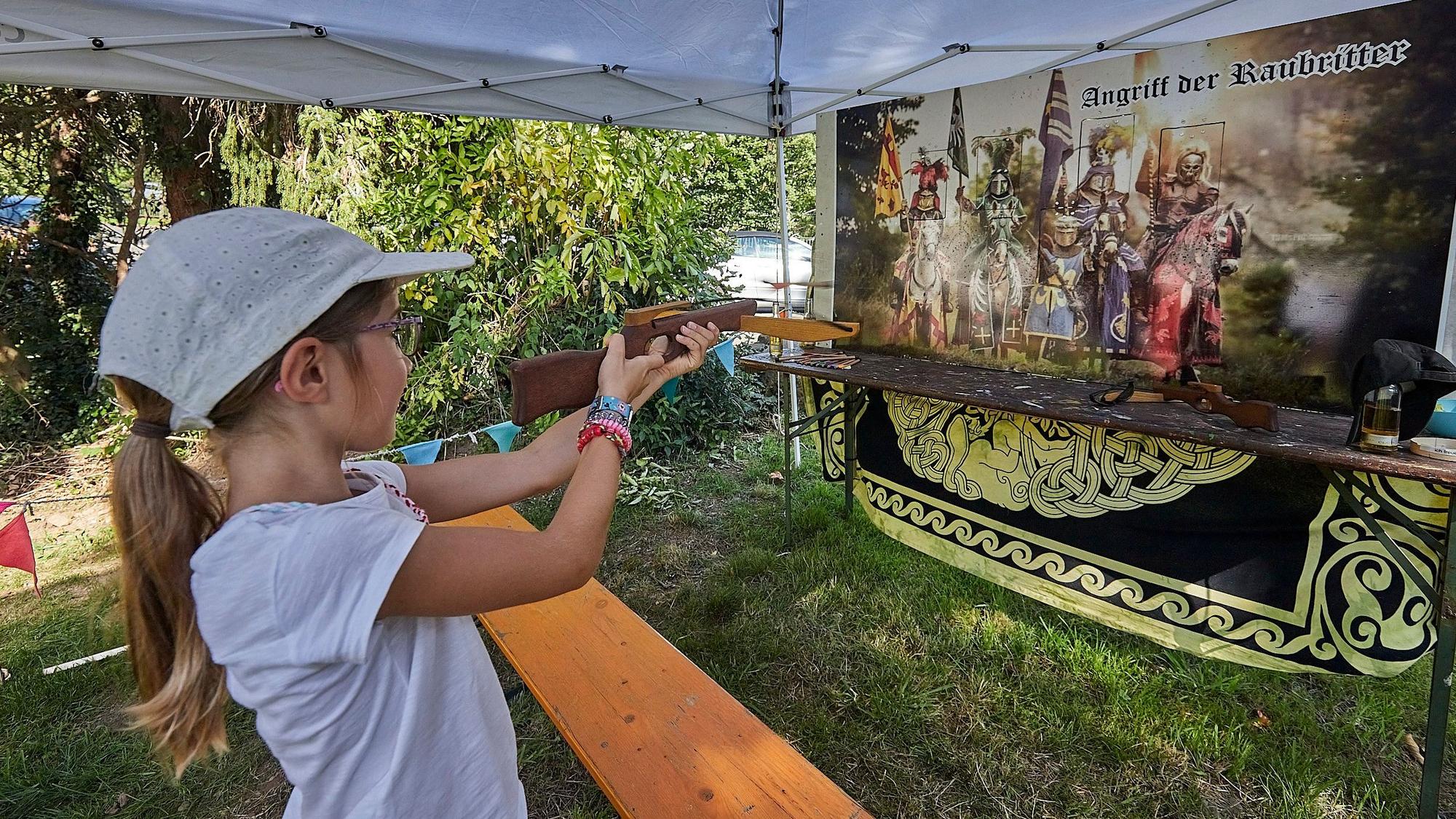 Ein Mädchen zielt bei einem Mittelalterfest mit einer Kinder-Armbrust auf ein Ziel.
