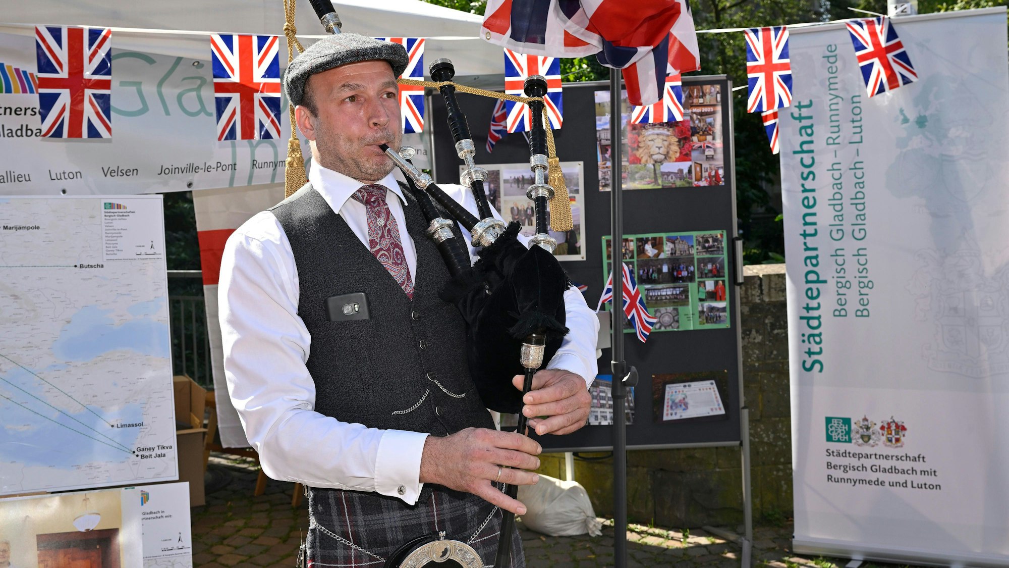 Dudelsackspieler Marc Steffen spielt vor einer Girlande aus Großbritannien-Fähnchen auf seinem Instrument.