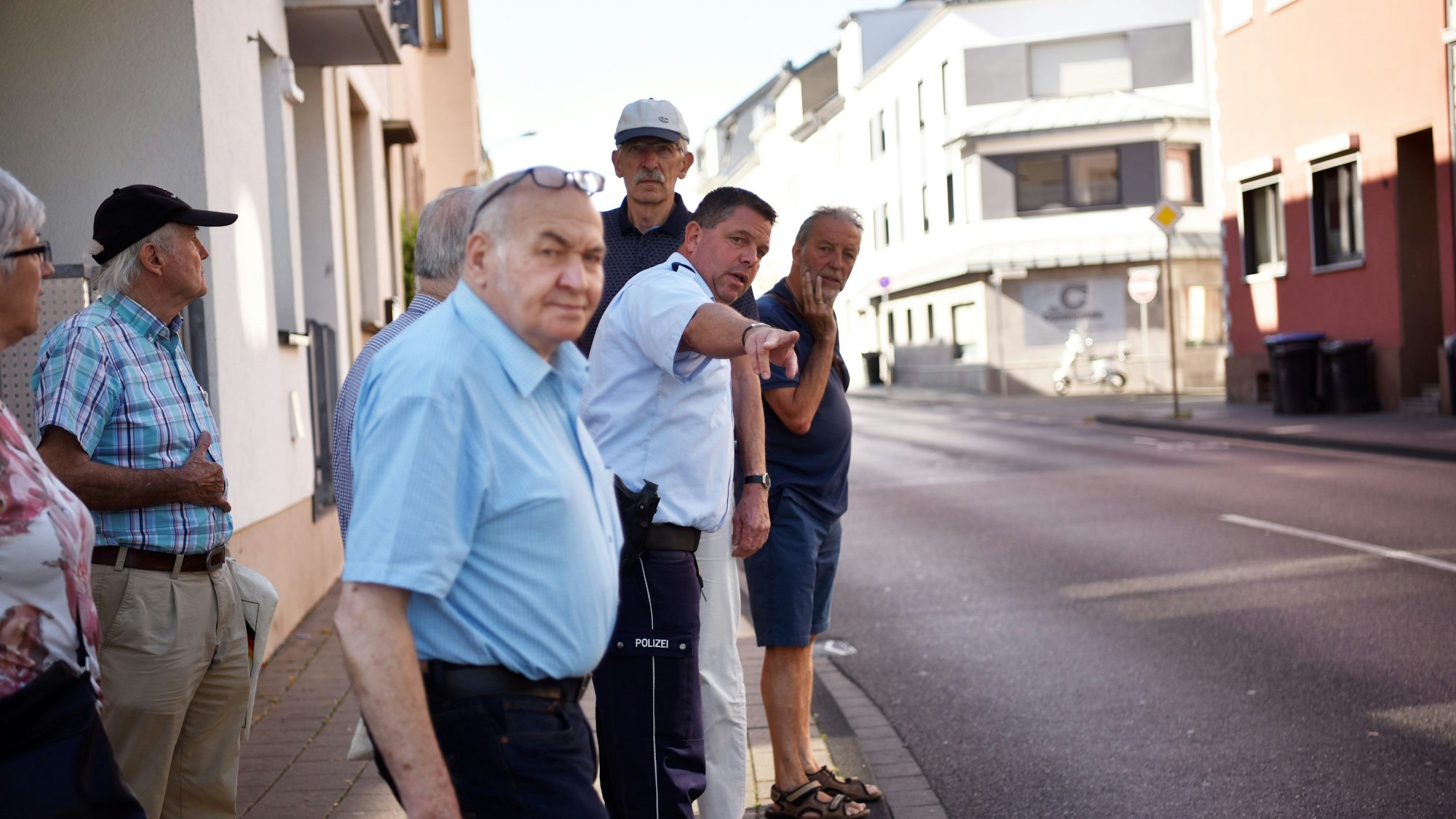 Ein Polizist steht mit Senioren und Seniorinnen in Euskirchen am Straßenrand und erklärt ihnen das richtige Verhalten im Straßenverkehr.