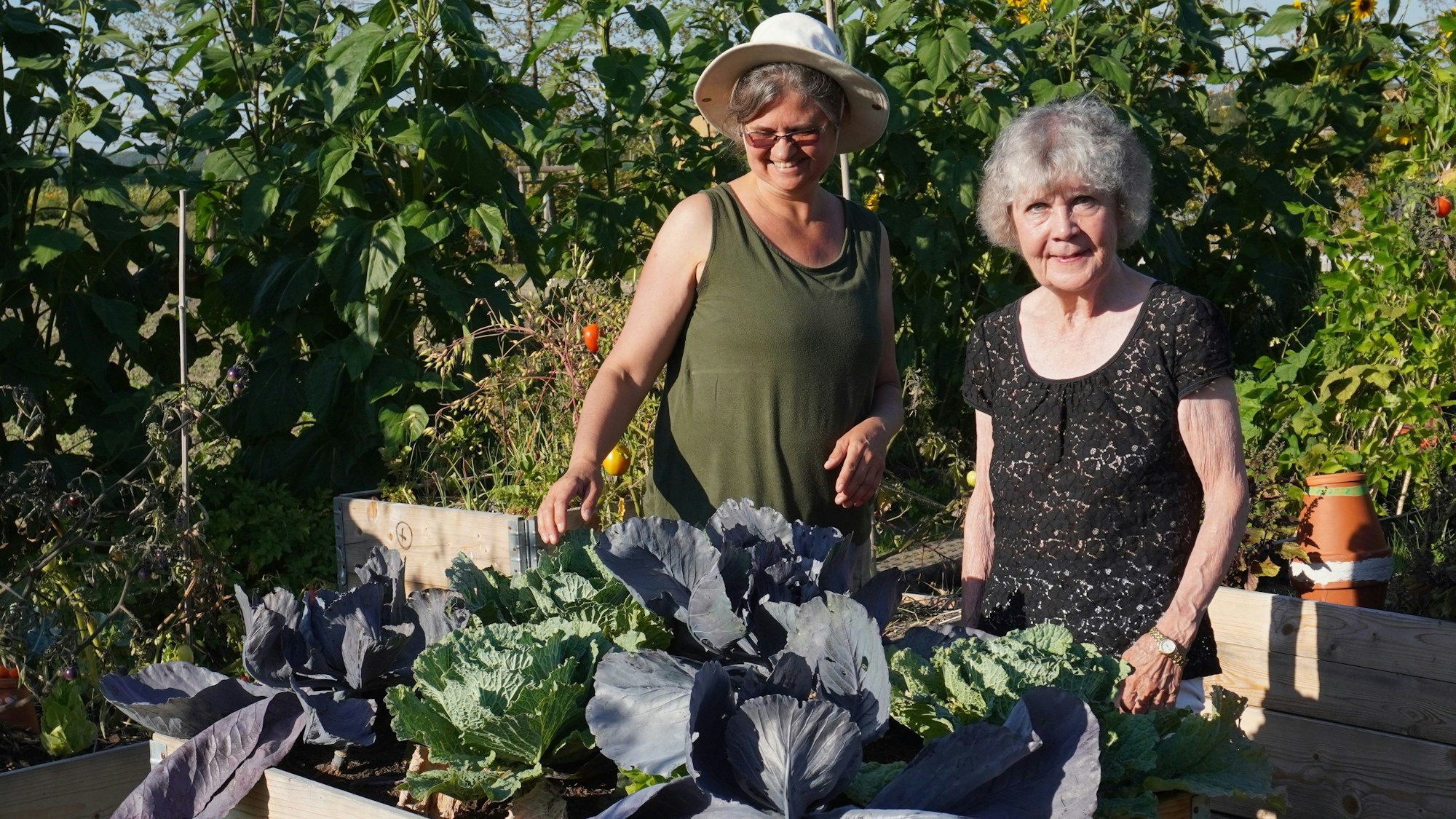 Zwei Frauen vor einem Hochbeet in einem Garten.