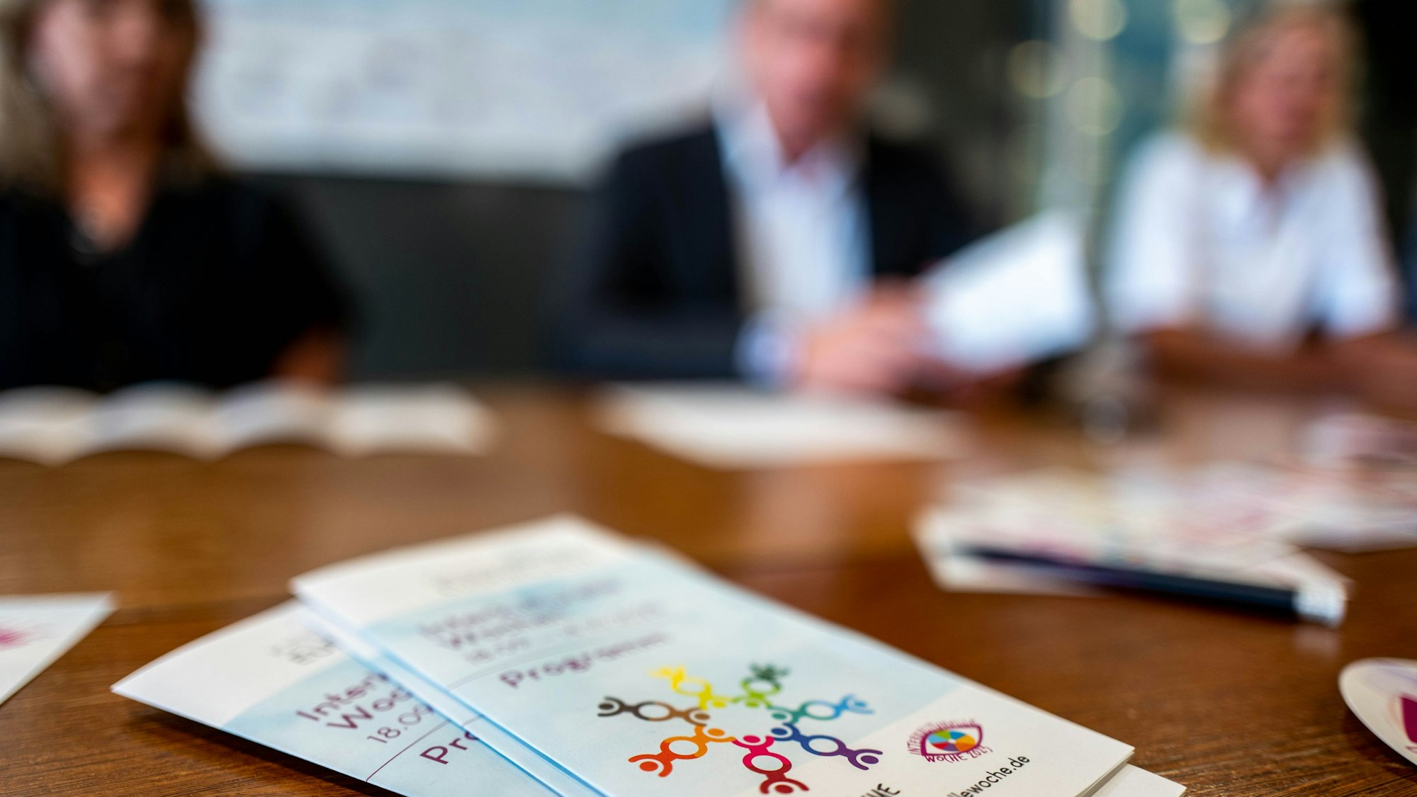 Das Bild zeigt den Flyer der Interkulturellen Wochen im Kreis Euskirchen. Im Hintergrund sind drei Menschen zu erahnen.