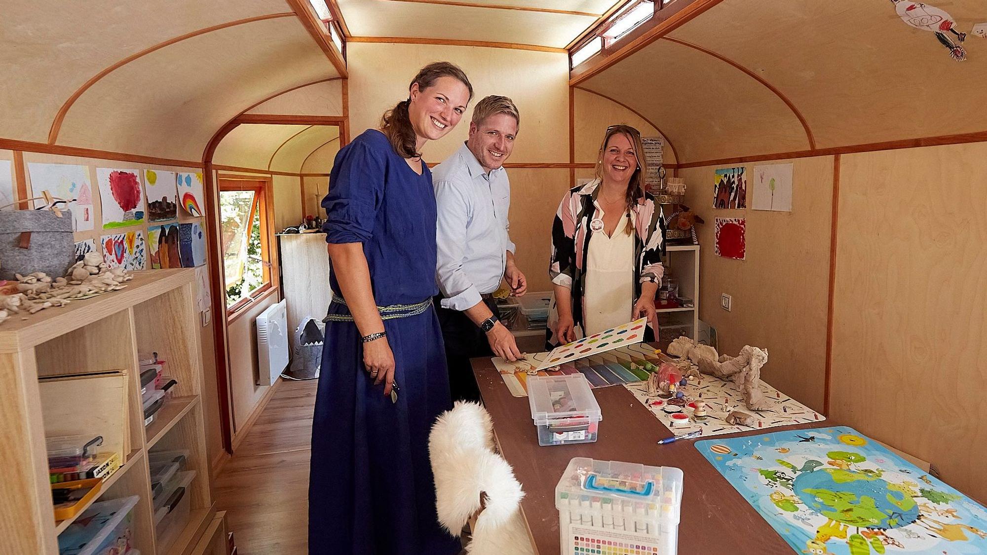 Landrat Markus Ramers, Rebecca Müller (links) und Klaudia Skodnik stehen in einem Bauwagen, der Spielmaterial und die Möglichkeit für Kreativangebote bietet.