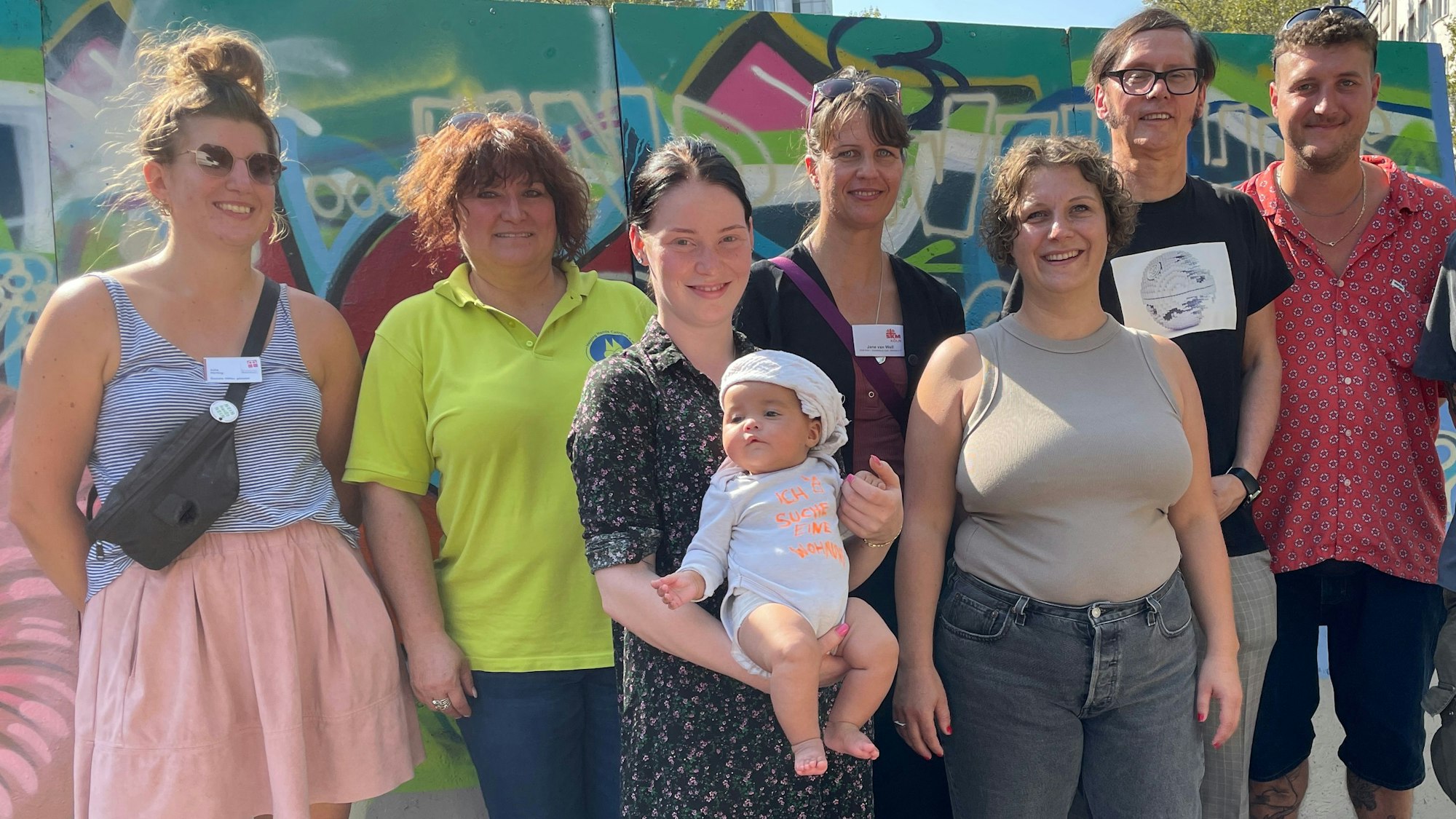 Alle stehen vor einer bunten Graffitiwand.