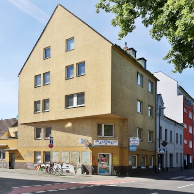 Ein sehr großes Eckhaus mit gelbem Anstrich und Ladenlokal im Erdgeschoss ist zu sehen.