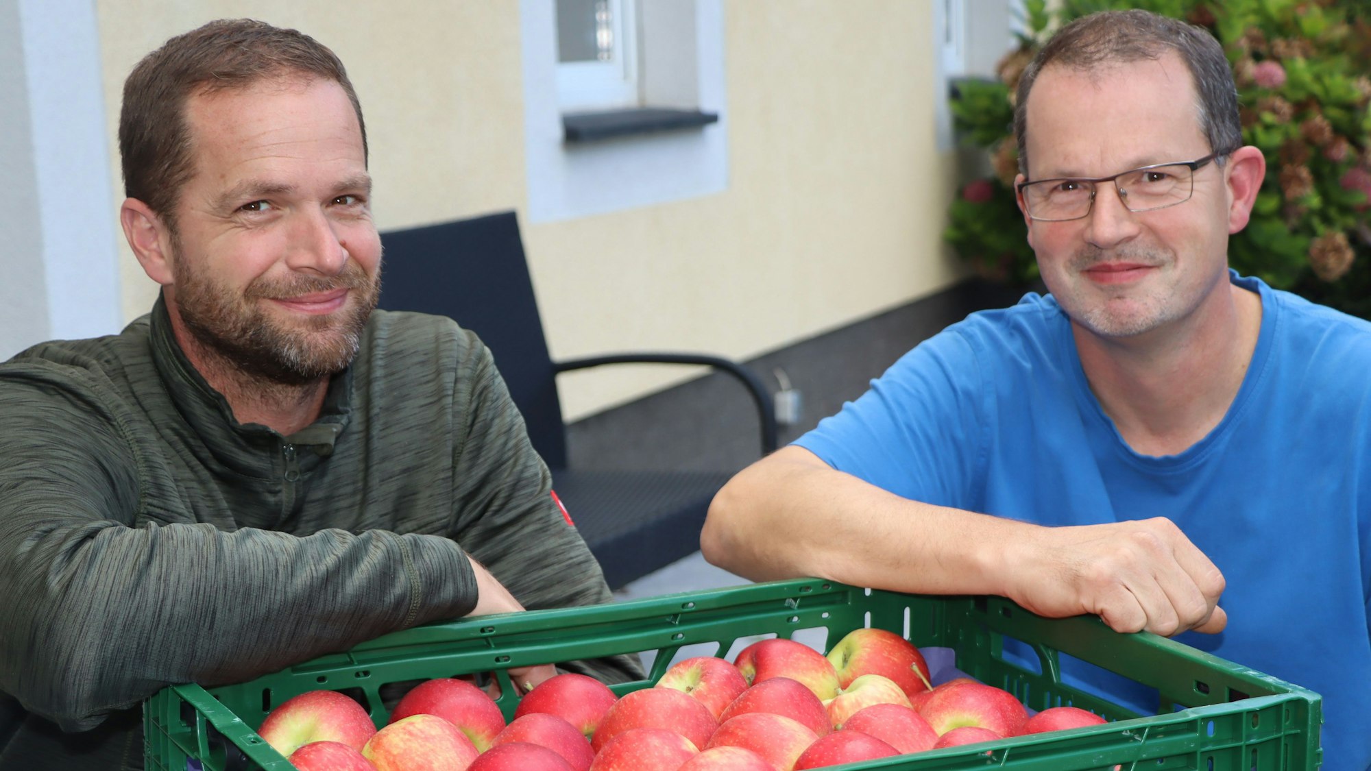 Auf dem Foto sind die Brüder Andreas und Michael Lettmann zu sehen. Sie stützen sich auf eine Kiste mit Äpfeln.