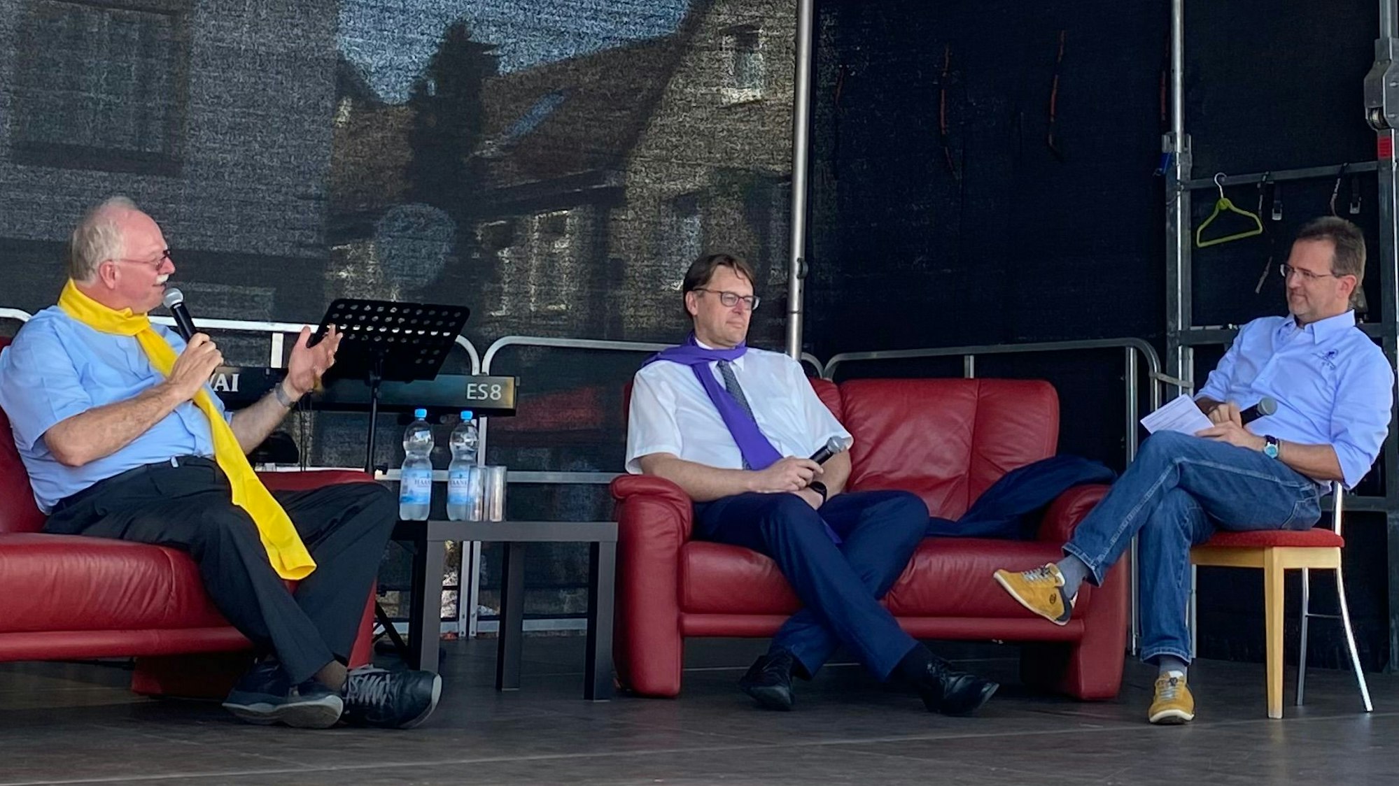 Drei Herren sitzen auf einem Podium und diskutieren.