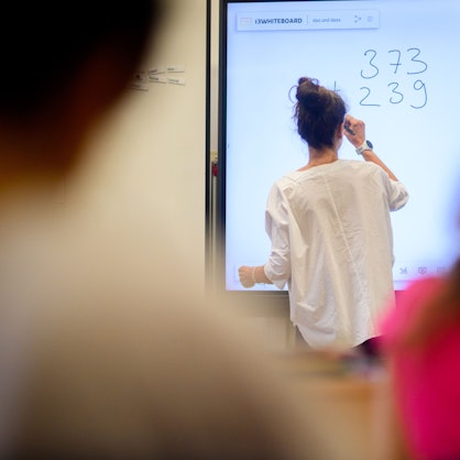 Ein Lehrerin schreibt eine Mathematikaufgabe auf eine digitale Schultafel im Klassenraum einer 4. Klasse einer Grundschule.