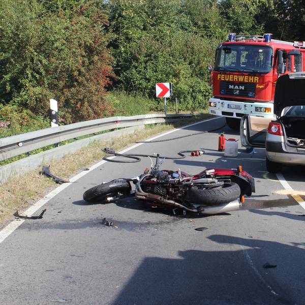 Ein schwer beschädigtes Motorrad liegt auf der Straße, dahinter stehen ein Auto sowie Einsatzfahrzeuge der Feuerwehr Kürten.