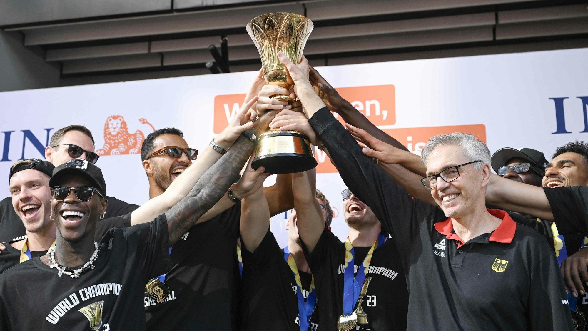 Die deutschen Basketball-Spieler um Dennis Schröder (l.) halten gemeinsam mit Coach Gordon Herbert ihren WM-Pokal hoch.