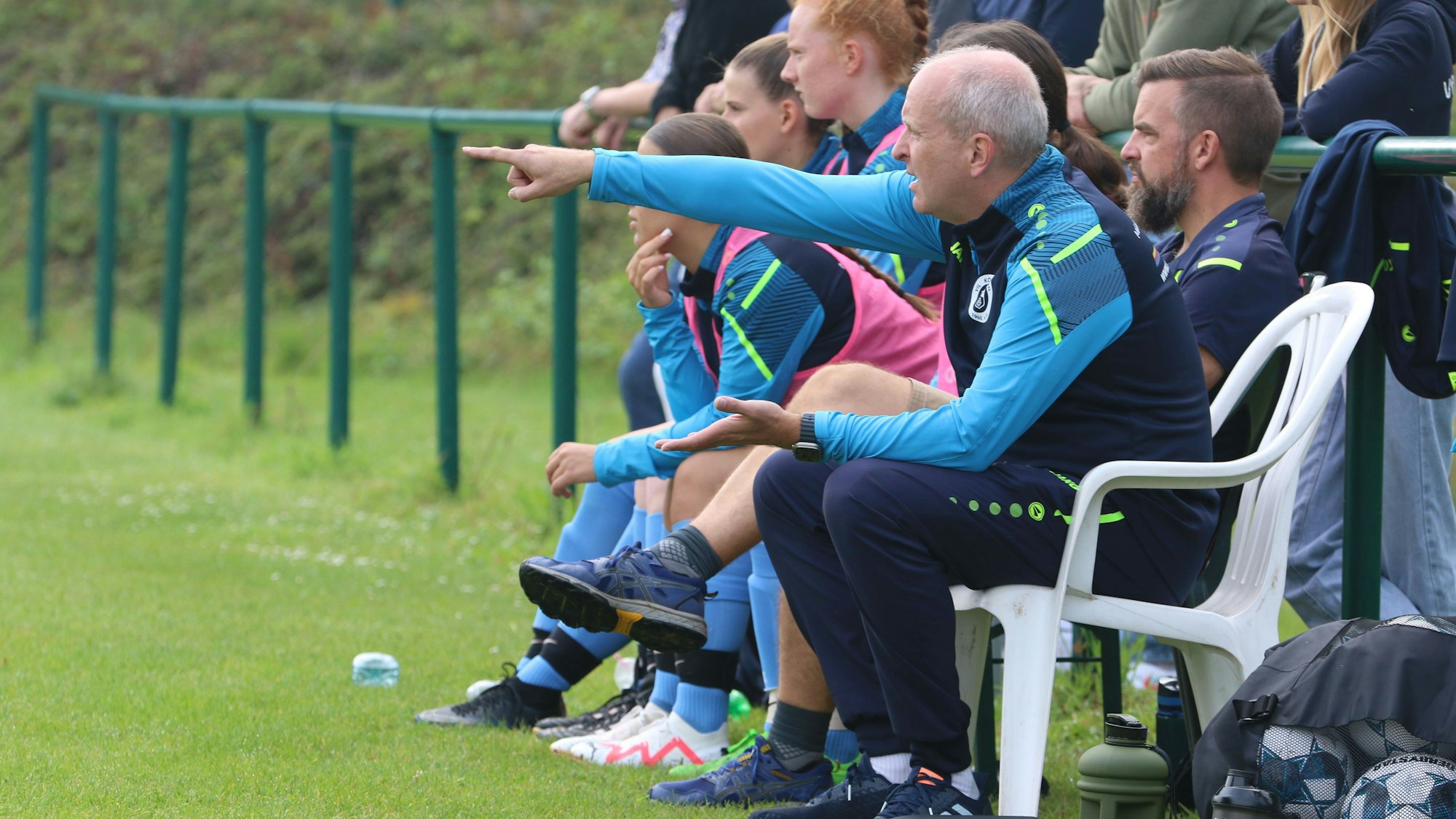 Das Bild zeigt Kommerns Trainer Sascha Wagner, wie er auf einem weißen Stuhl sitzt und Richtung Tor zeigt.