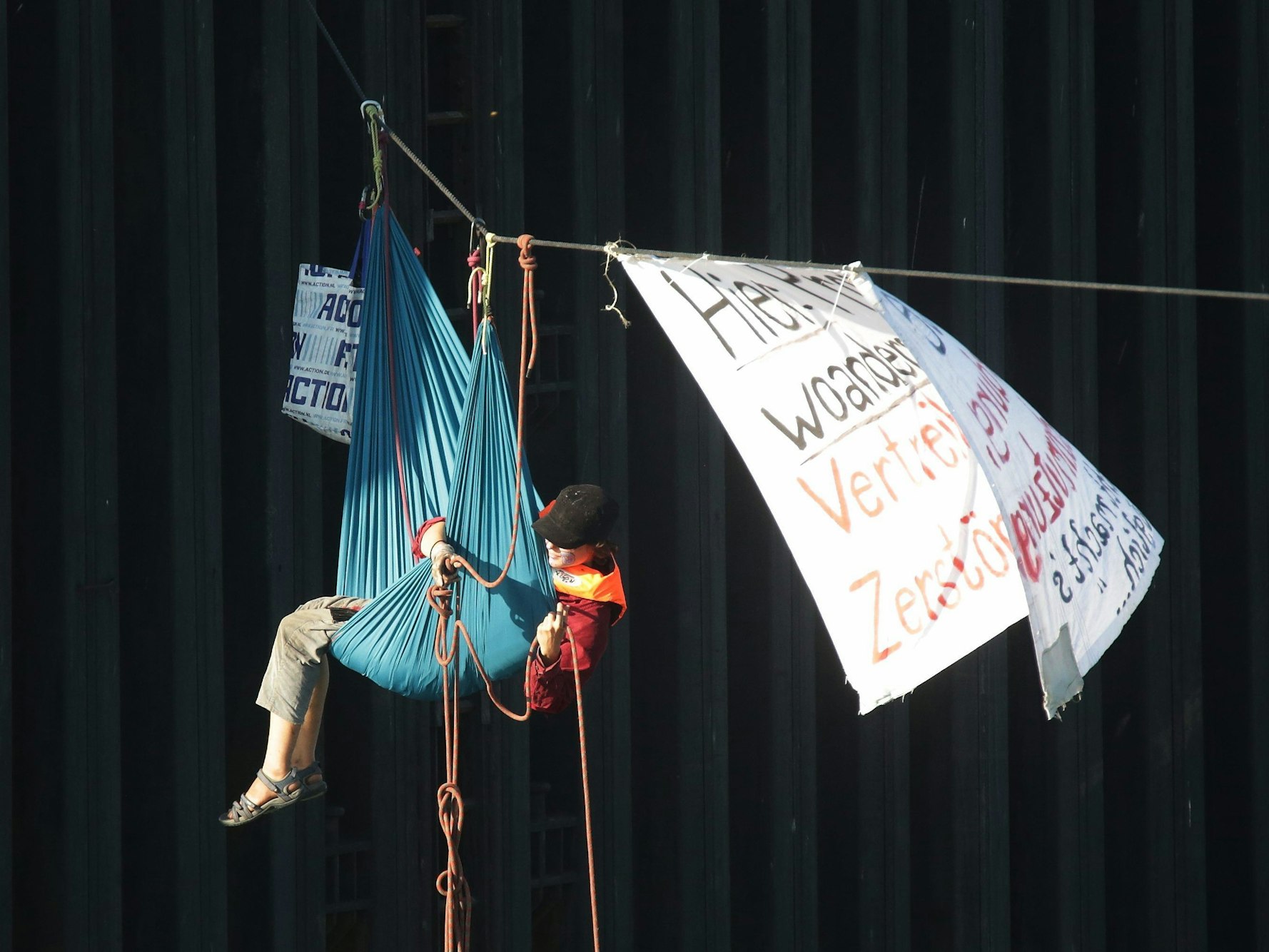 Eine Aktivistin in einer Hängematte am Seil blockiert die Hafen-Zufahrt zur Shell-Raffinerie Wesseling im Godorfer Rhein-Hafen.
