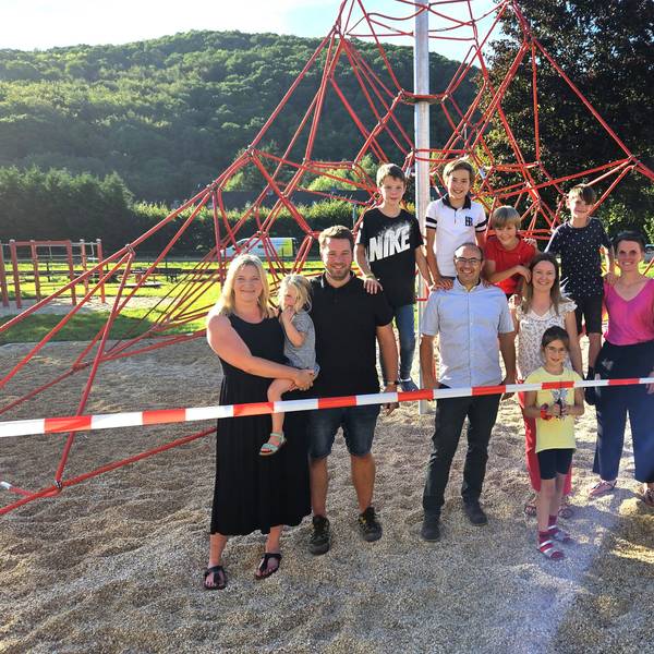 Eine Gruppe aus Kindern und Erwachsenen steht an und auf einer Kletterpyramide aus roten Seilen.