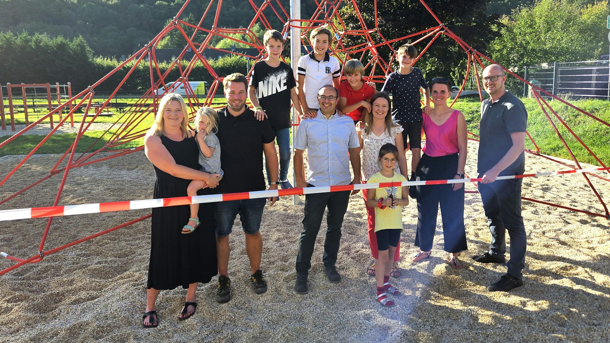 Eine Gruppe aus Kindern und Erwachsenen steht an und auf einer Kletterpyramide aus roten Seilen.