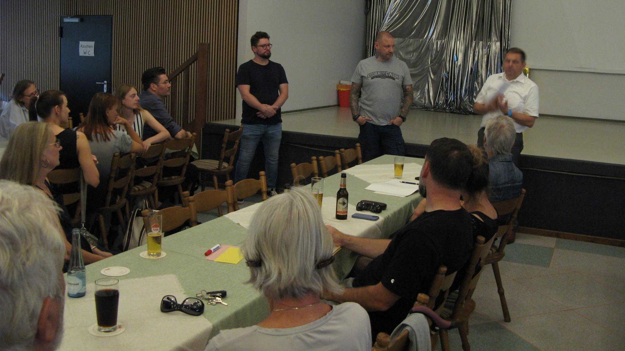 In Saal sitzen Menschen an Tischen, vorn stehen drei Männer, die den Verein „Hennef Power“ vorstellen.