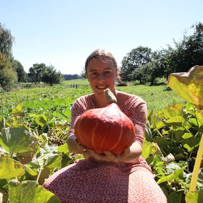 Pauline Gödecke von der solidarischen Landwirtschaft in Much hält auf einem Feld einen orangefarbenen Kürbis in die Kamera