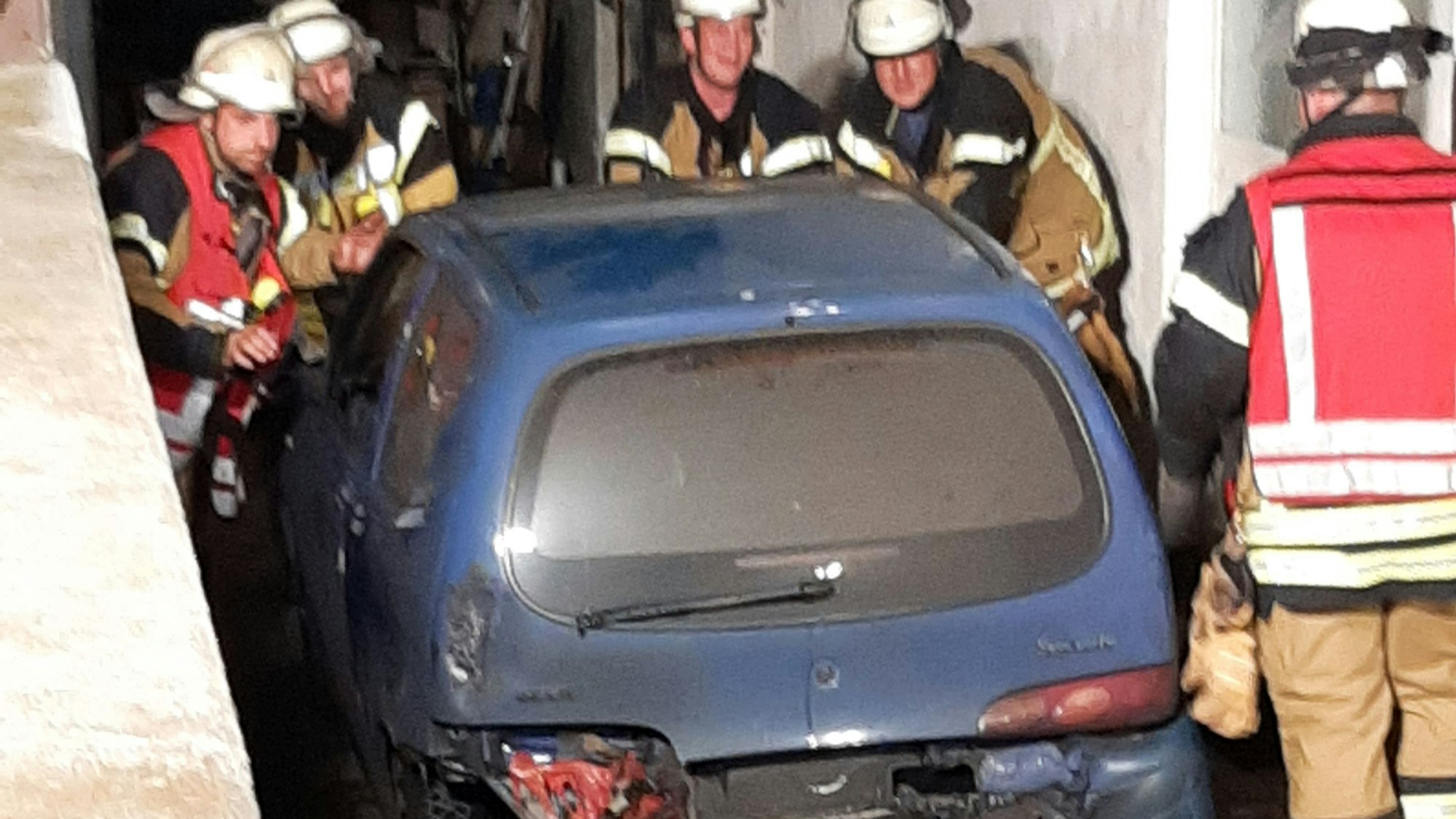 Einige Feuerwehrleute schieben einen blauen Kleinwagen aus einer Garage.