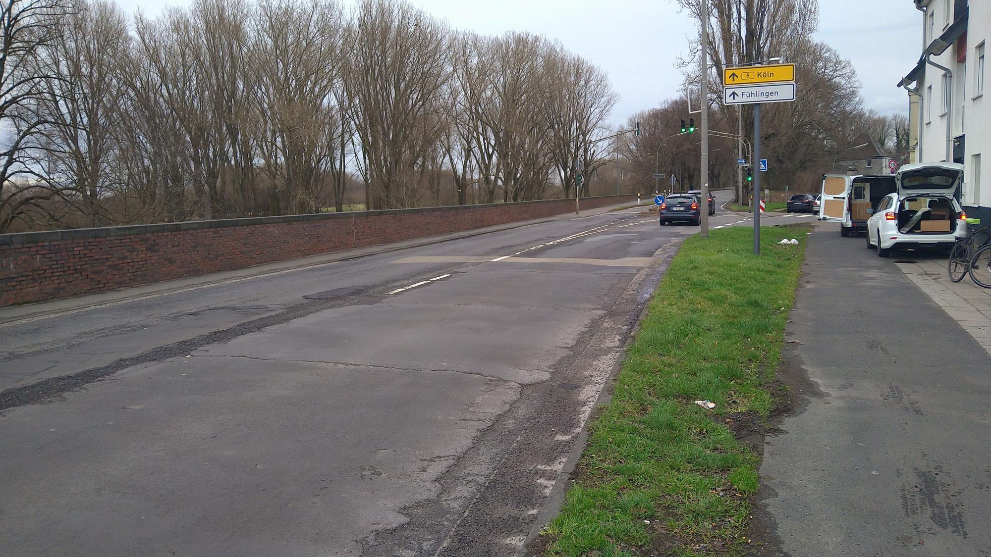 Blick auf eine Landstraße, am Rand sind eine Mauer und Bäume.