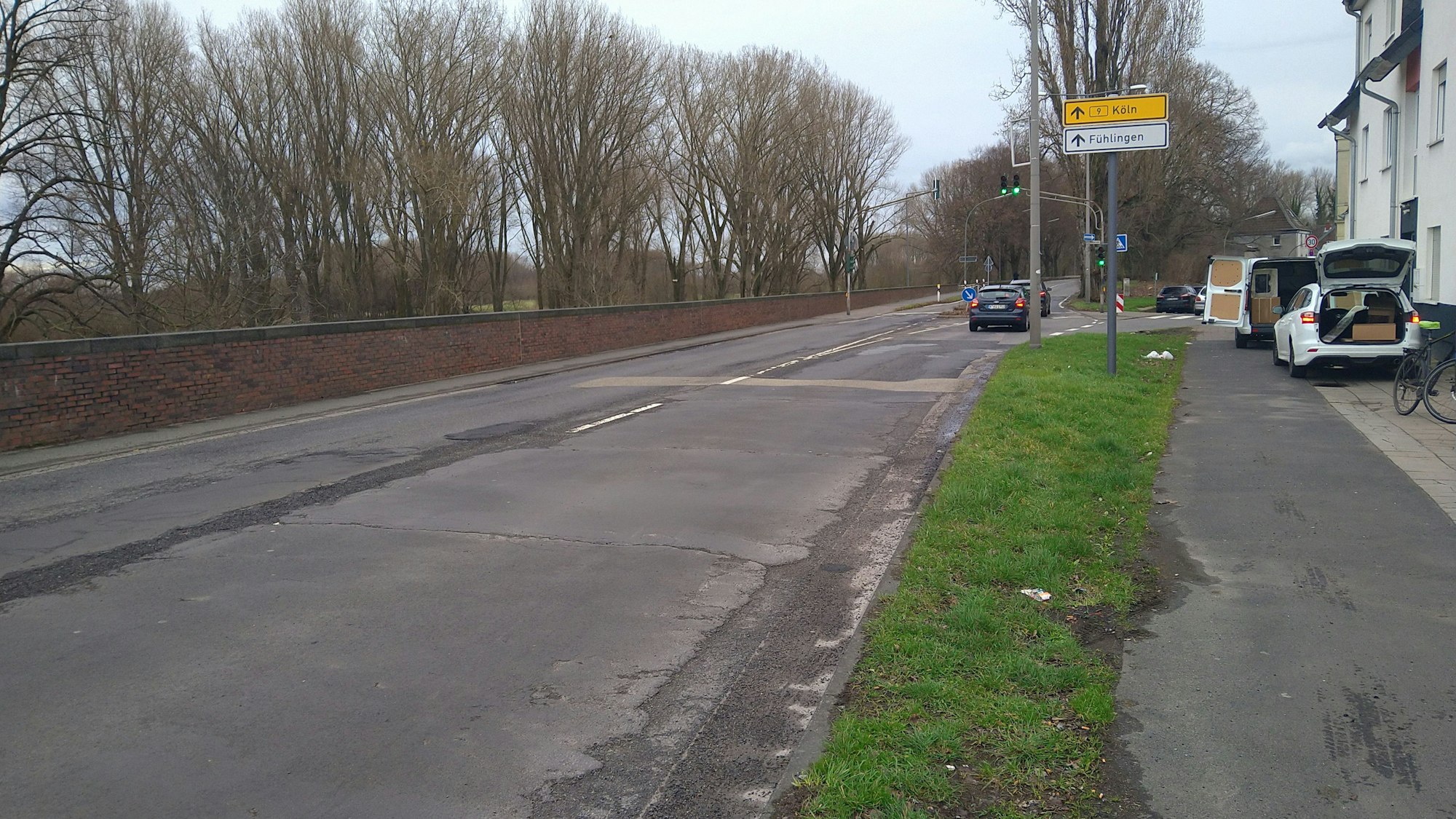 Blick auf eine Landstraße, am Rand sind eine Mauer und Bäume.