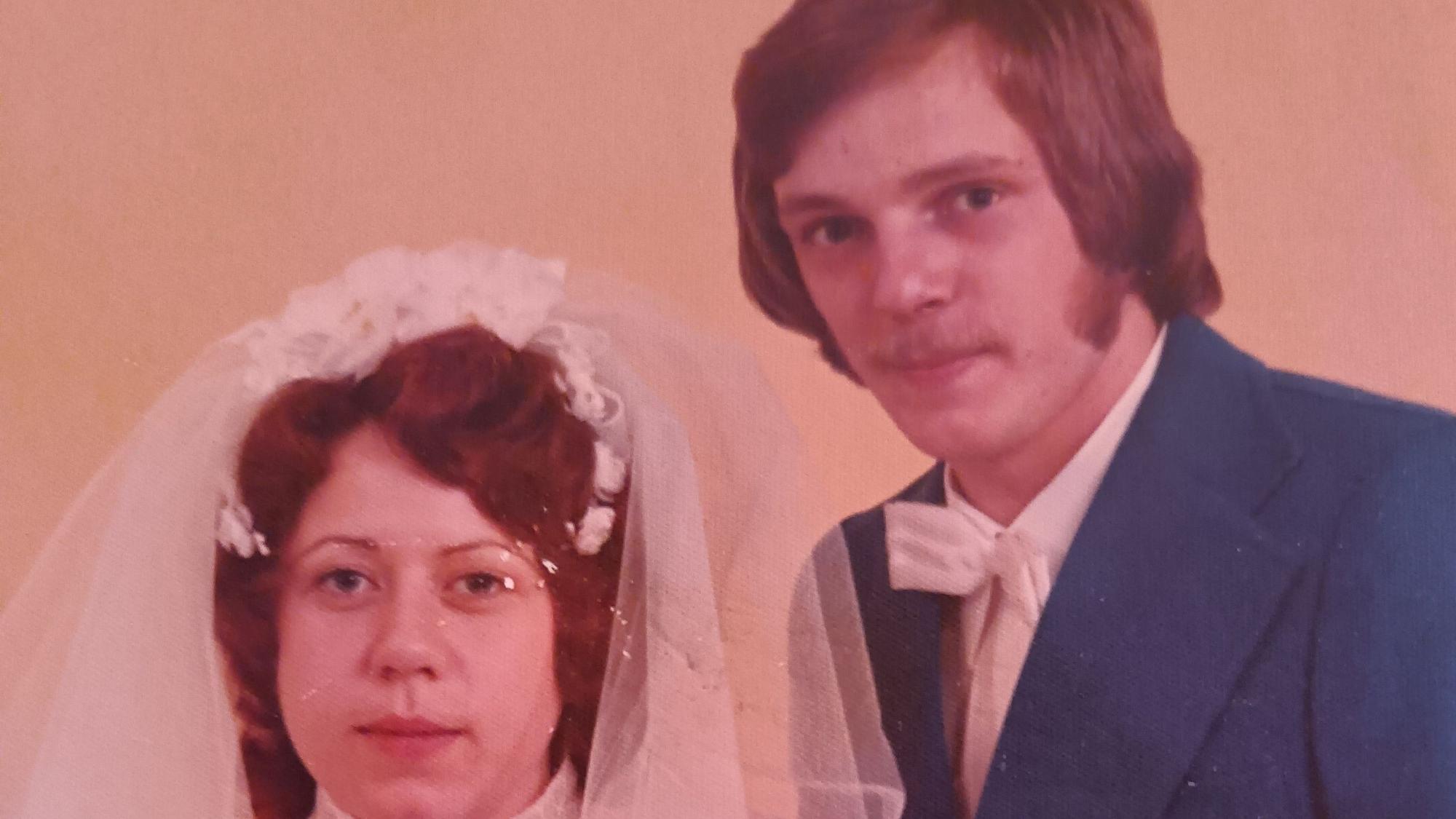 Eine Frau im Hochzeitskleid und ein Mann im Anzug und mit weißer Fliege posieren für ein Foto.