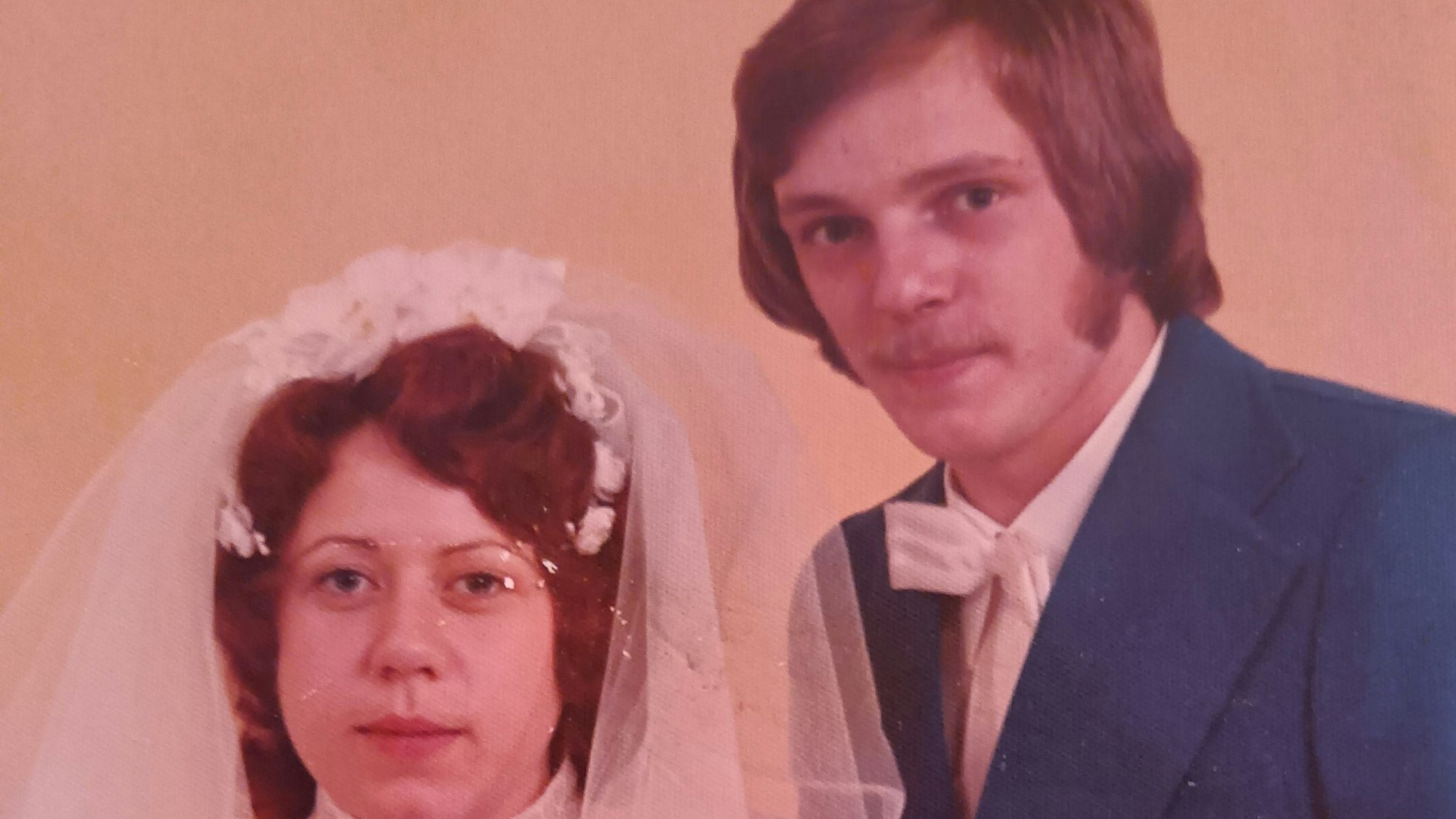 Eine Frau im Hochzeitskleid und ein Mann im Anzug und mit weißer Fliege posieren für ein Foto.