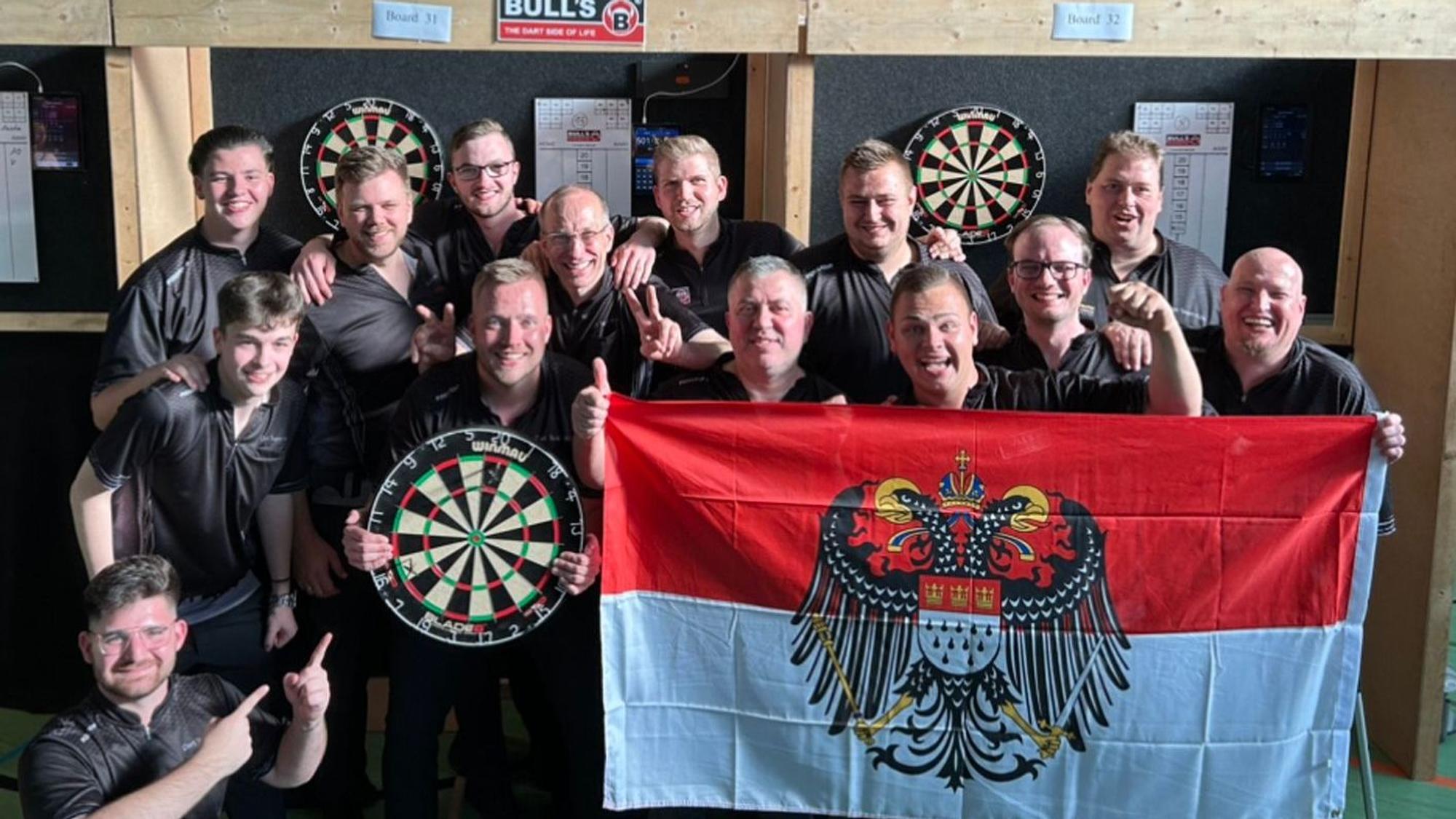 So sehen Sieger aus: Das Dartteam Köln feiert den Aufstieg. Im Dartboard stecken noch die Pfeile mit den entscheidenden letzten Treffern.