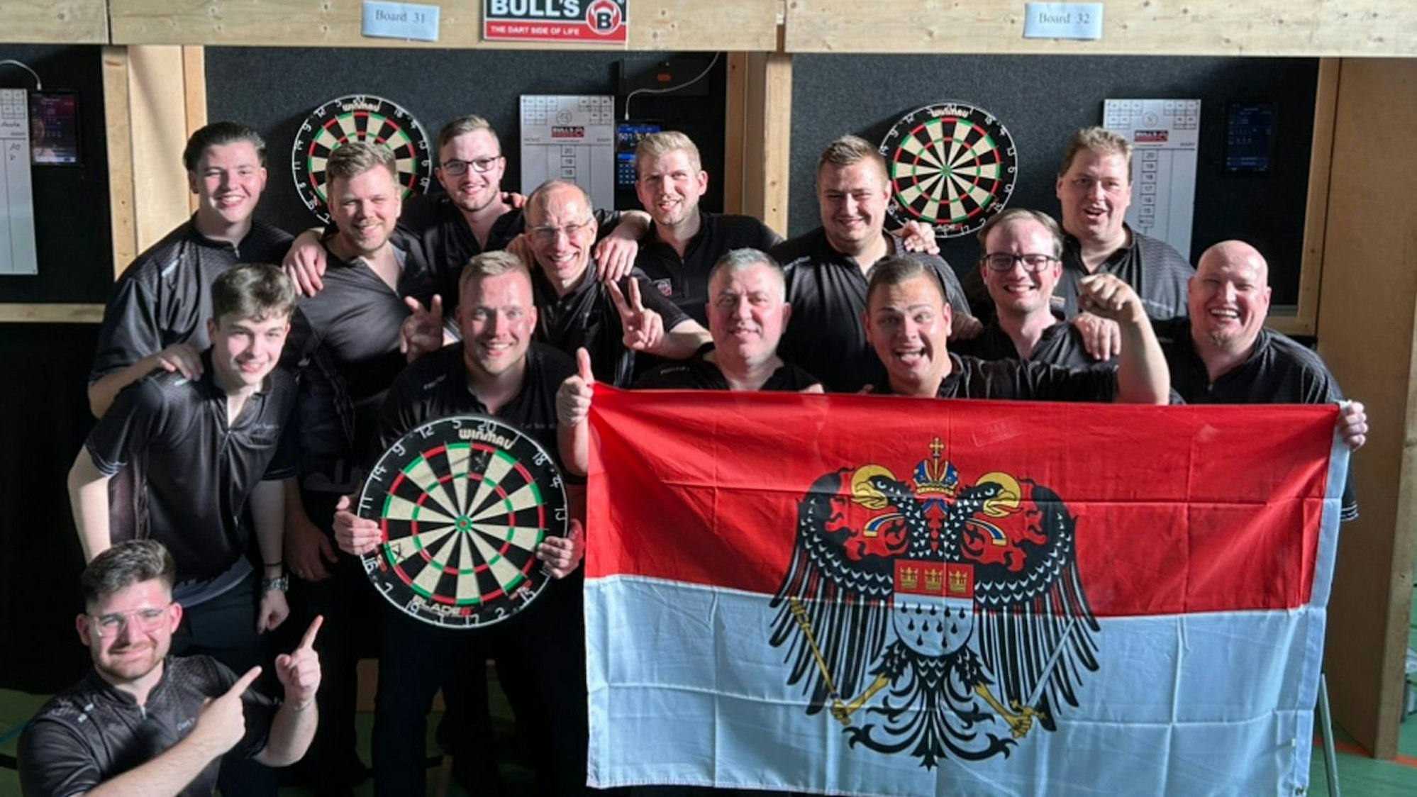 So sehen Sieger aus: Das Dartteam Köln feiert den Aufstieg. Im Dartboard stecken noch die Pfeile mit den entscheidenden letzten Treffern.
