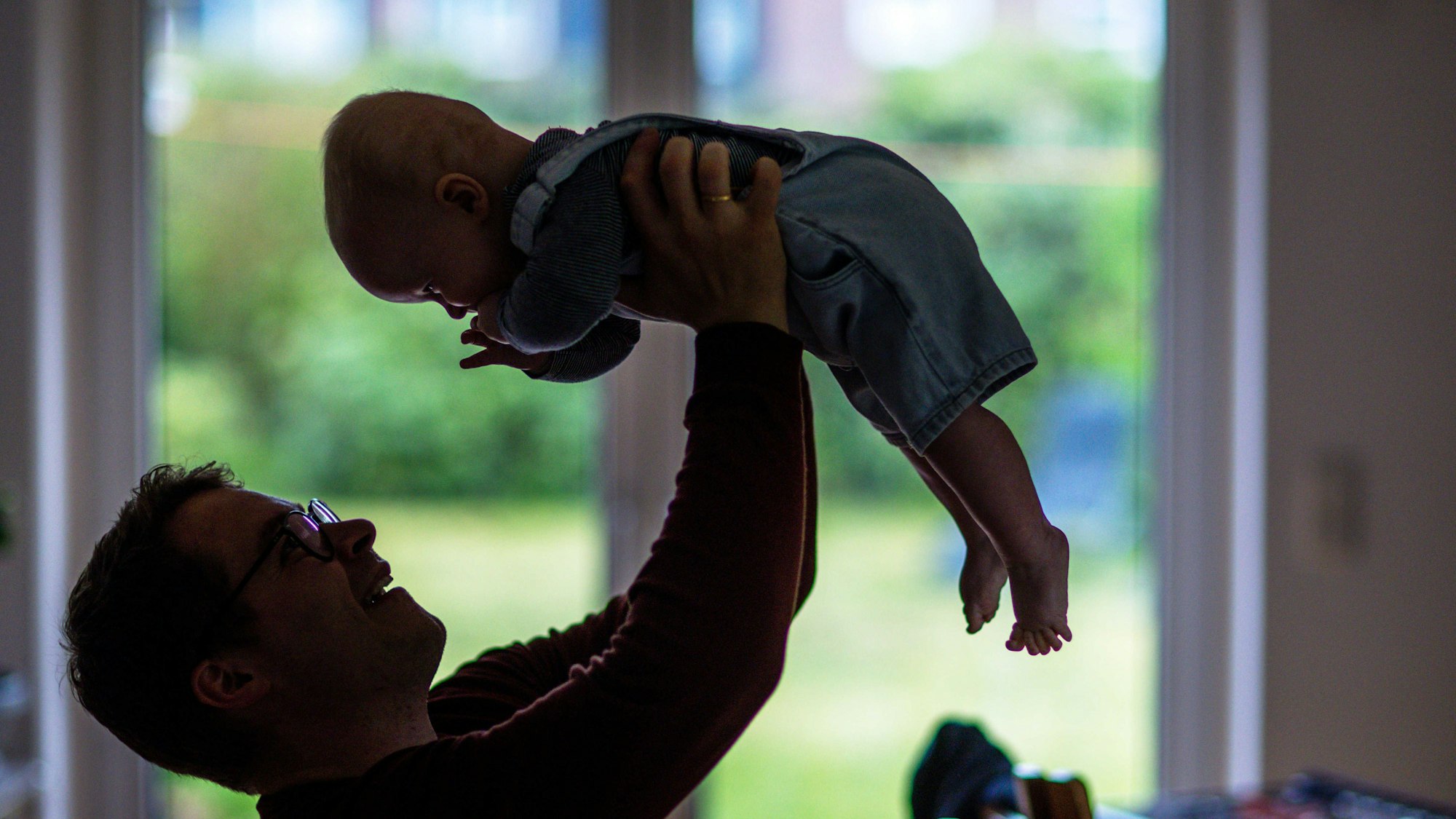 Ein junger Vater spielt mit seinem sechs Monate alten Sohn im Wohnzimmer.