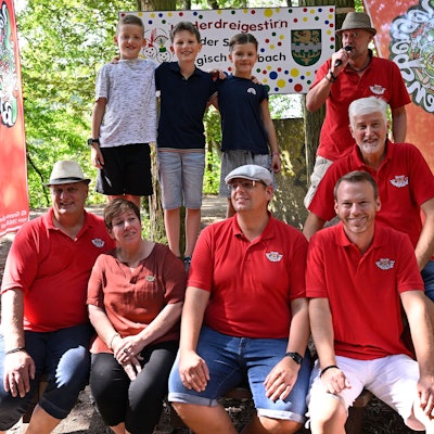 Das angehende Kinderdreigestirn der Kreisstadt Bergisch Gladbach steht im Wald vor einem Schild mit der Aufschrift „Kinderdreigestirn der Stadt Bergisch Gladbach“.
