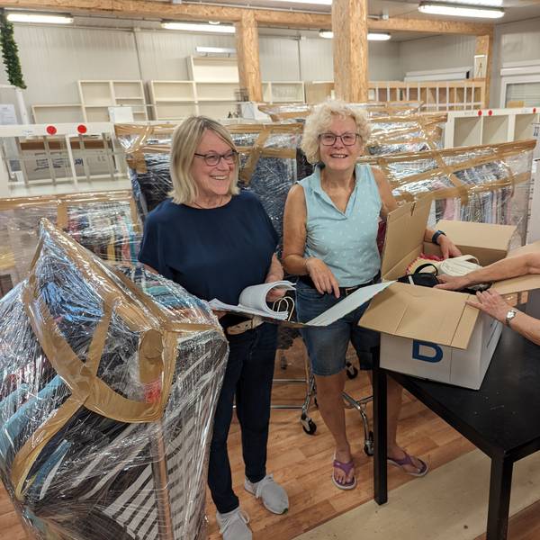 Zwei Frauen packen einen Karton, eine schaut in eine Liste vor leer geräumten Regalen.
