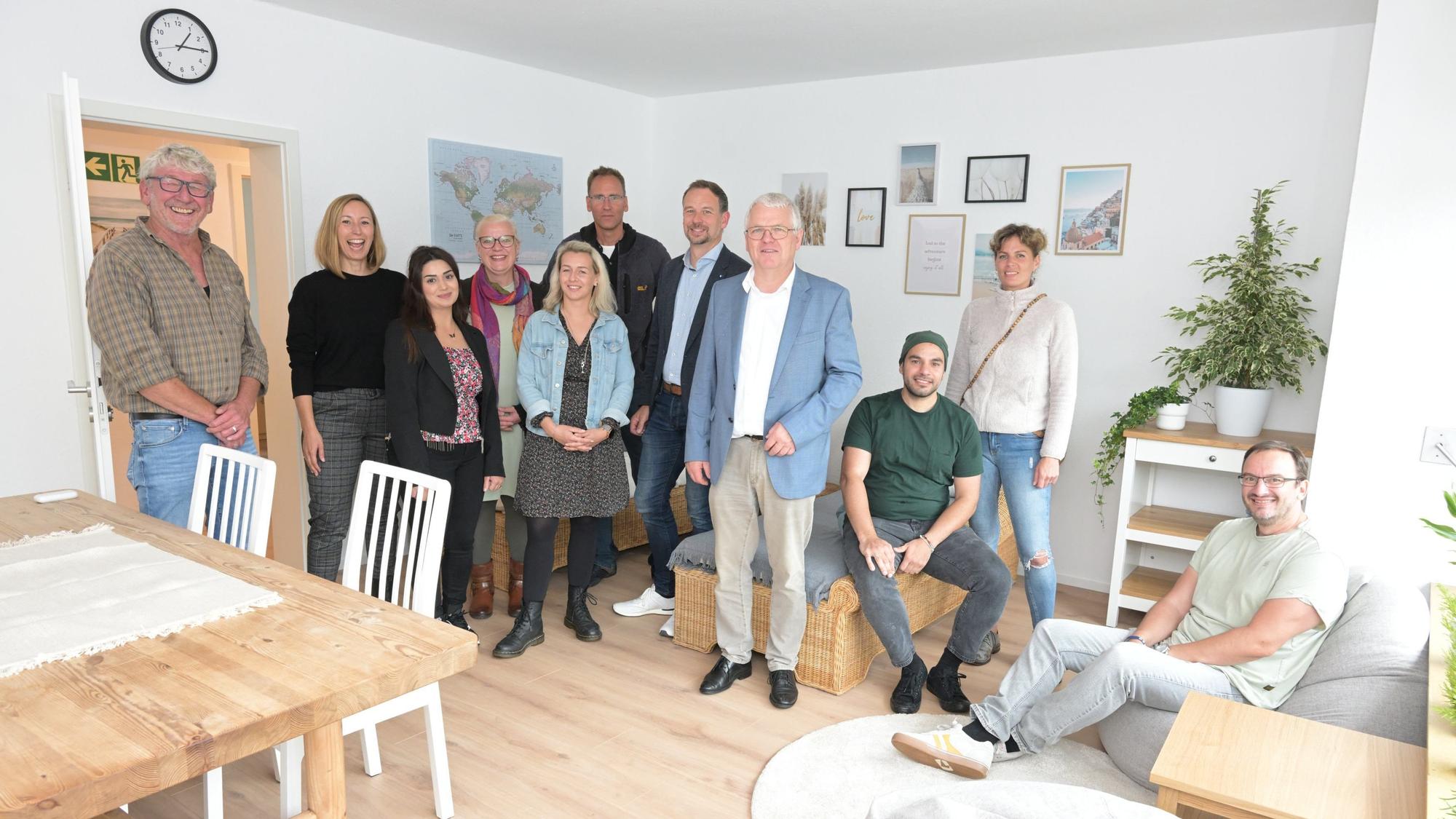 Elf Menschen stehen in einem hell eingerichteten Wohnraum in Kürten-Broich, der von einer Wohngruppe genutzt werden soll.