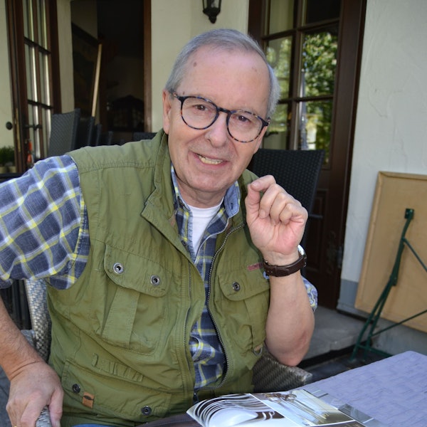 Günter Allmann sitzt in Reichshof-Hespert an einem Tisch und zeigt Bilder seiner Koch-Stationen.